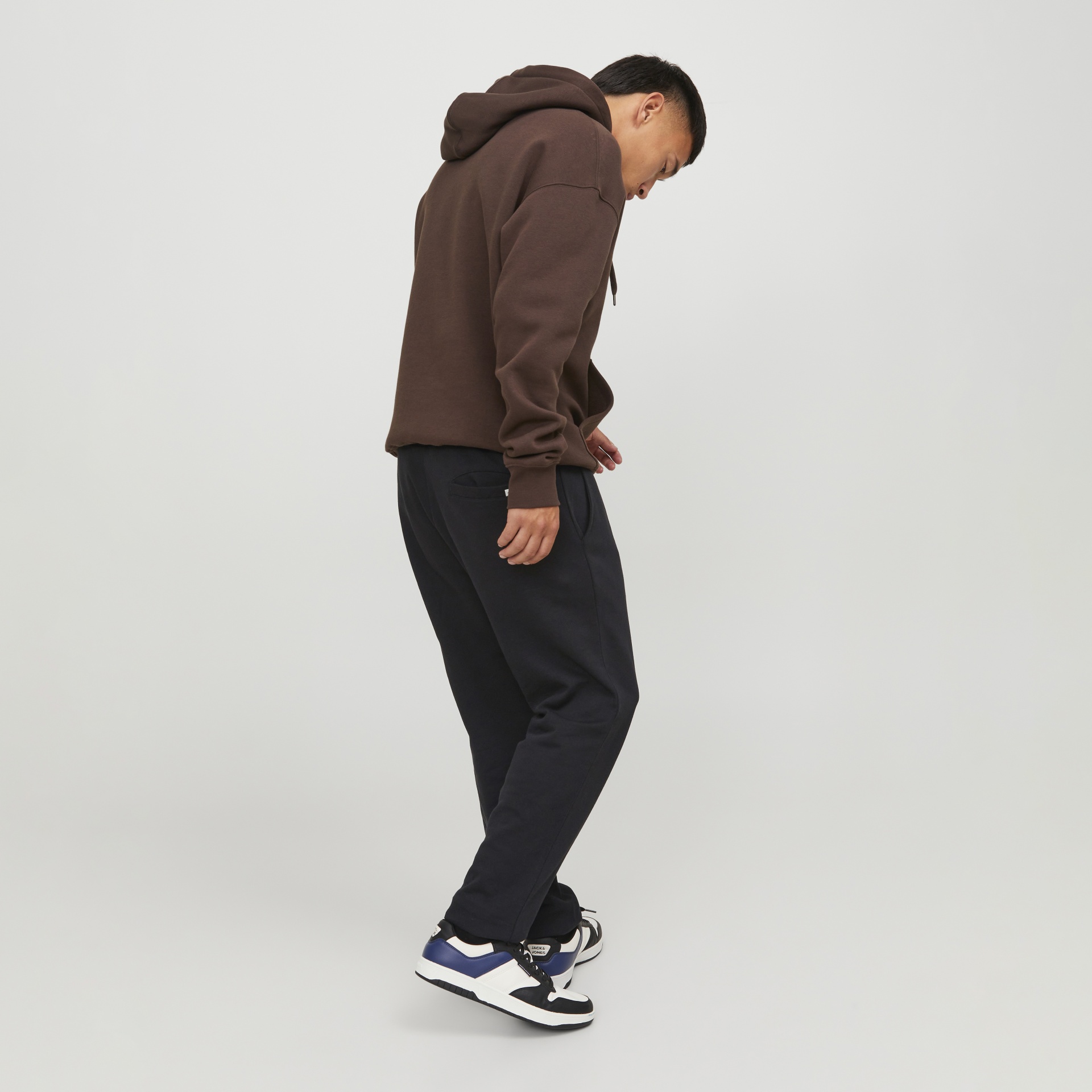 Homem de perfil com hoodie castanho e sapatilhas JACK & JONES.