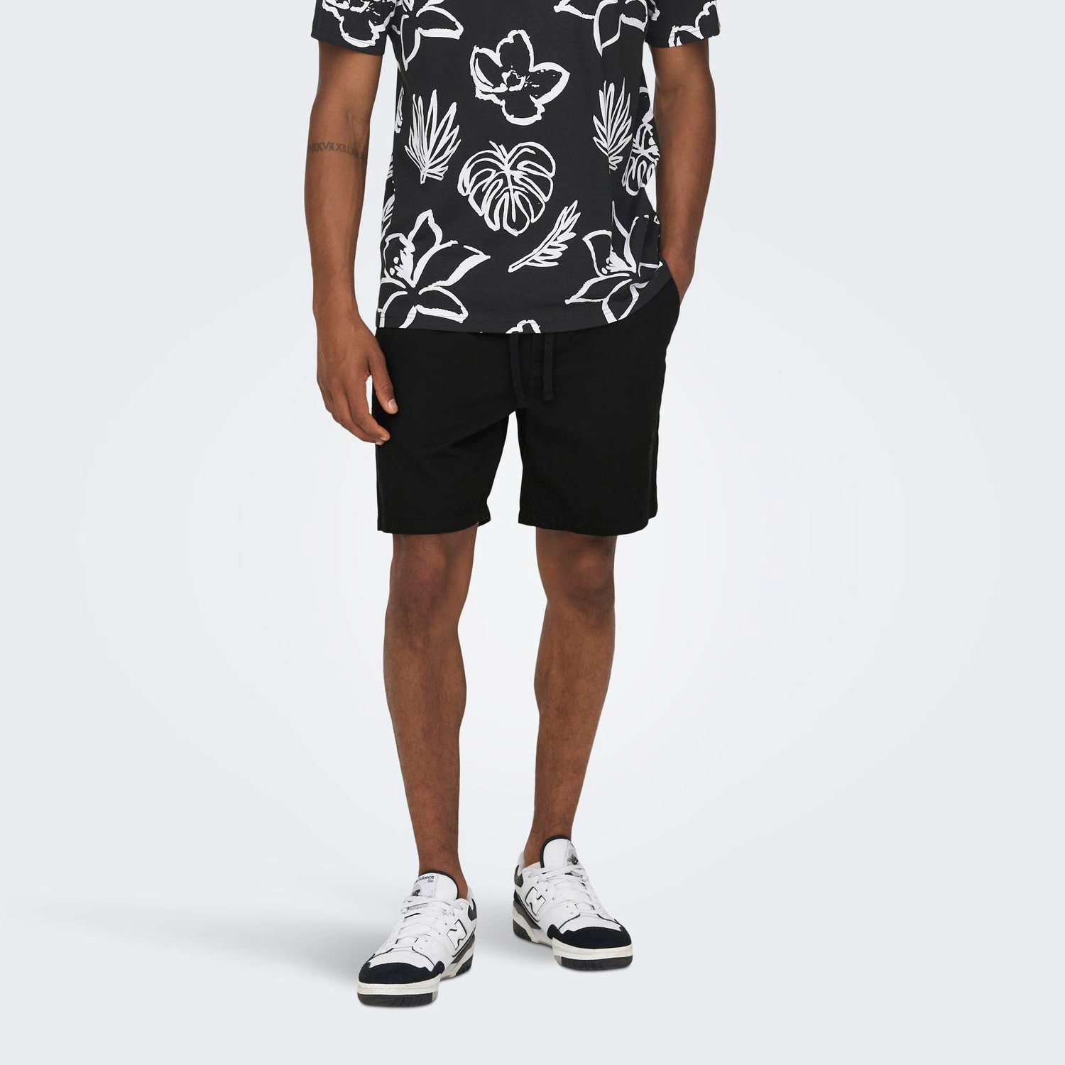 Homem a usar calções pretos, ténis brancos e t-shirt preta com padrão floral