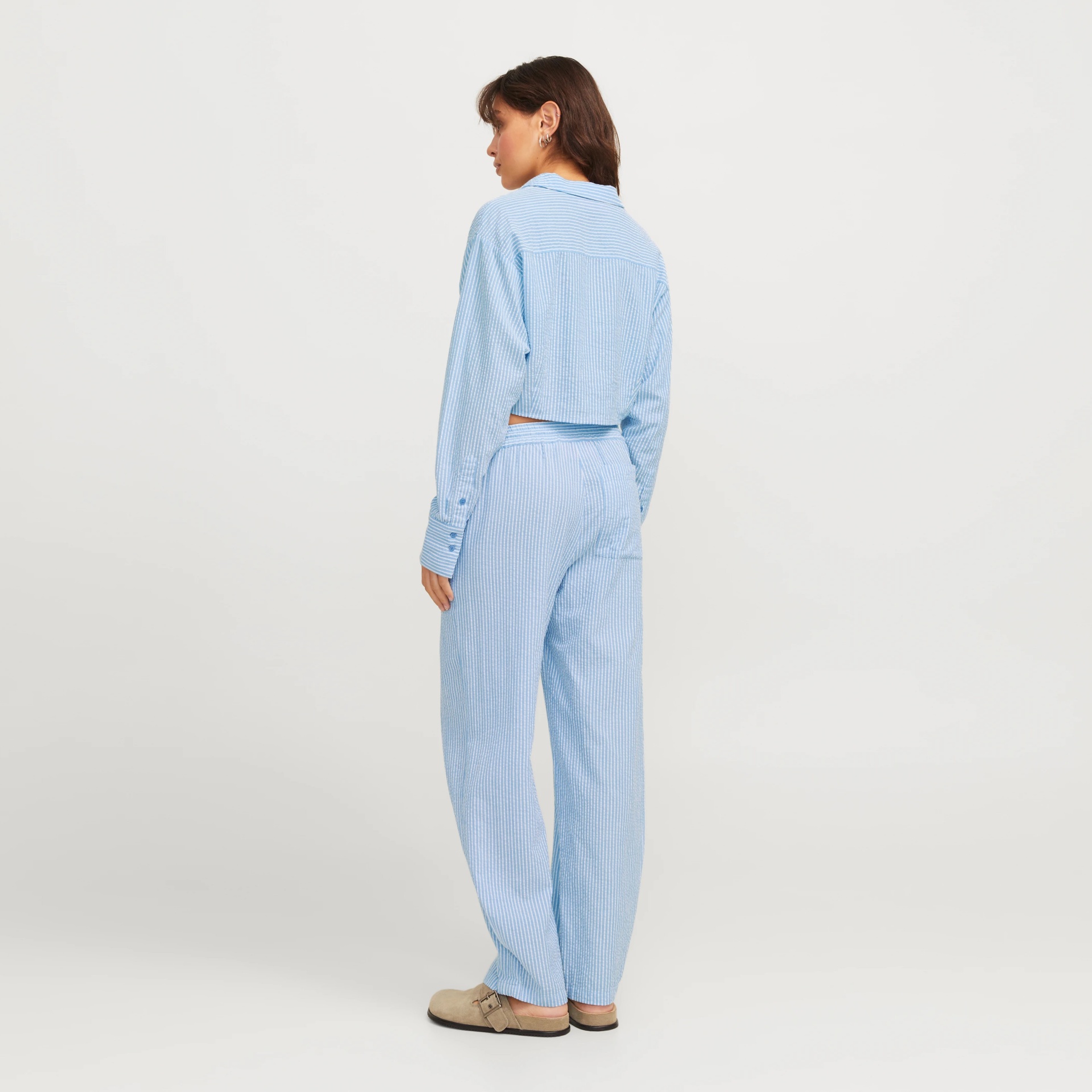 Mulher de costas vestindo conjunto azul claro com riscas brancas e calçado bege