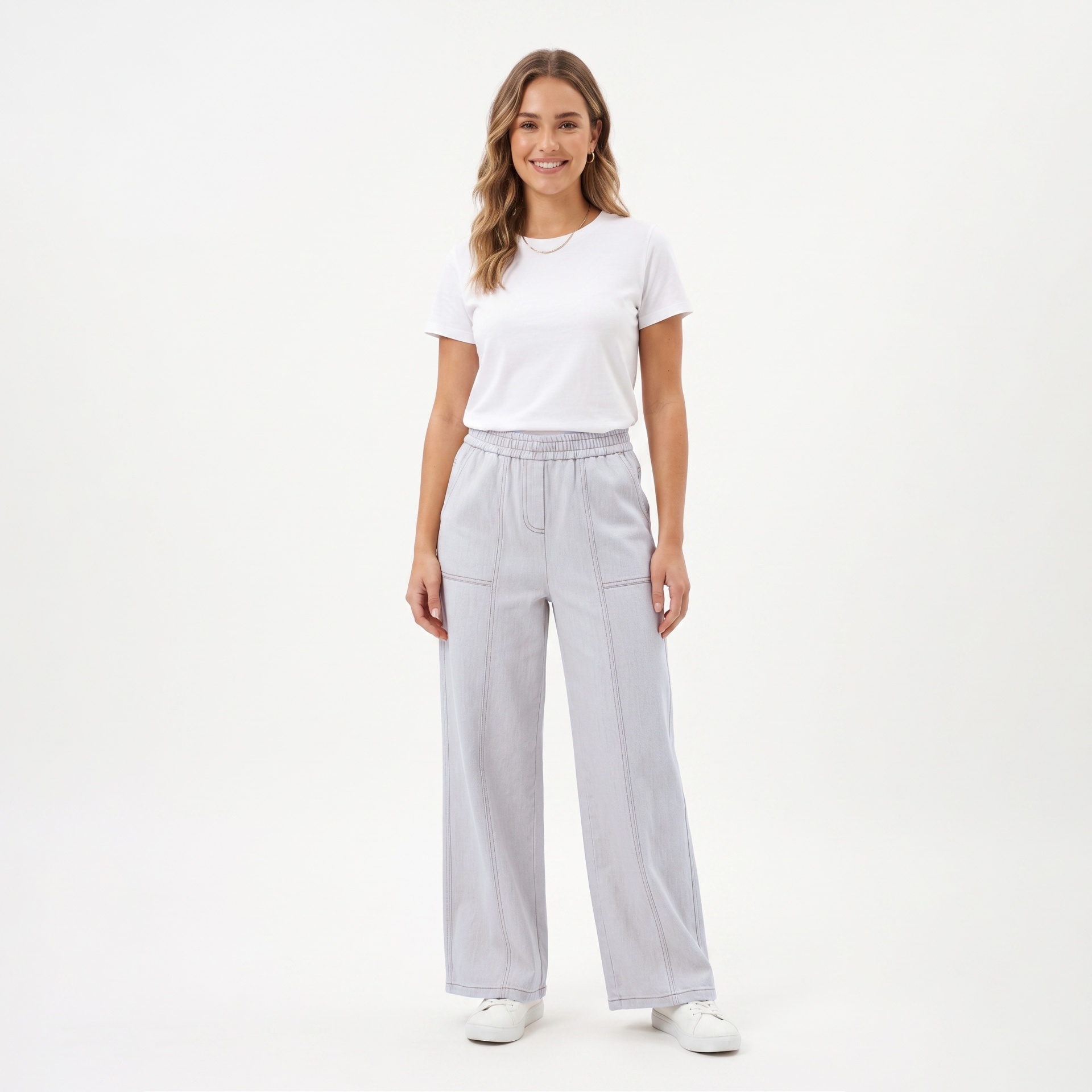Mulher com t-shirt branca, calças cinza claro e ténis brancos em fundo branco.