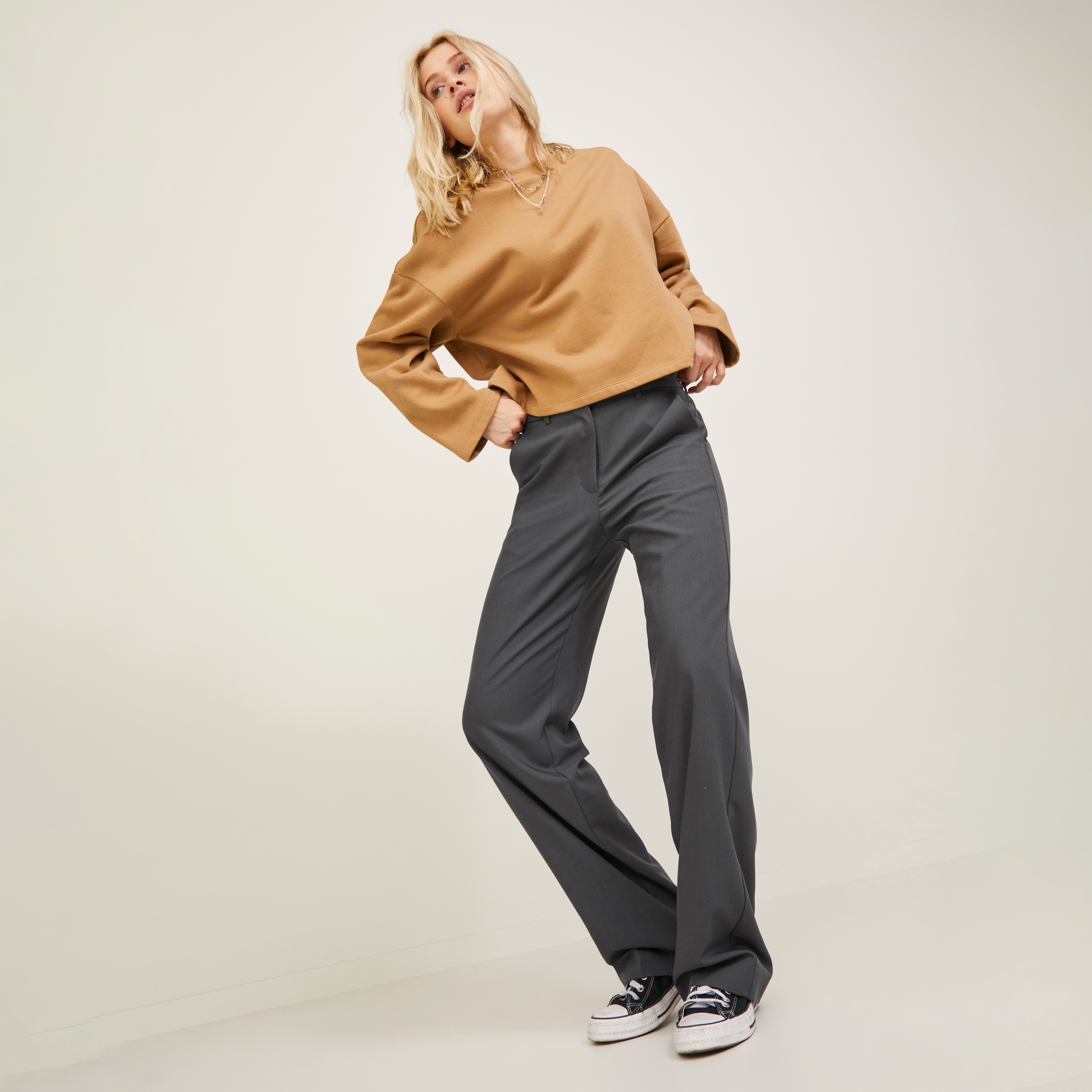 Mulher com roupa castanha e cinza posando em fundo neutro