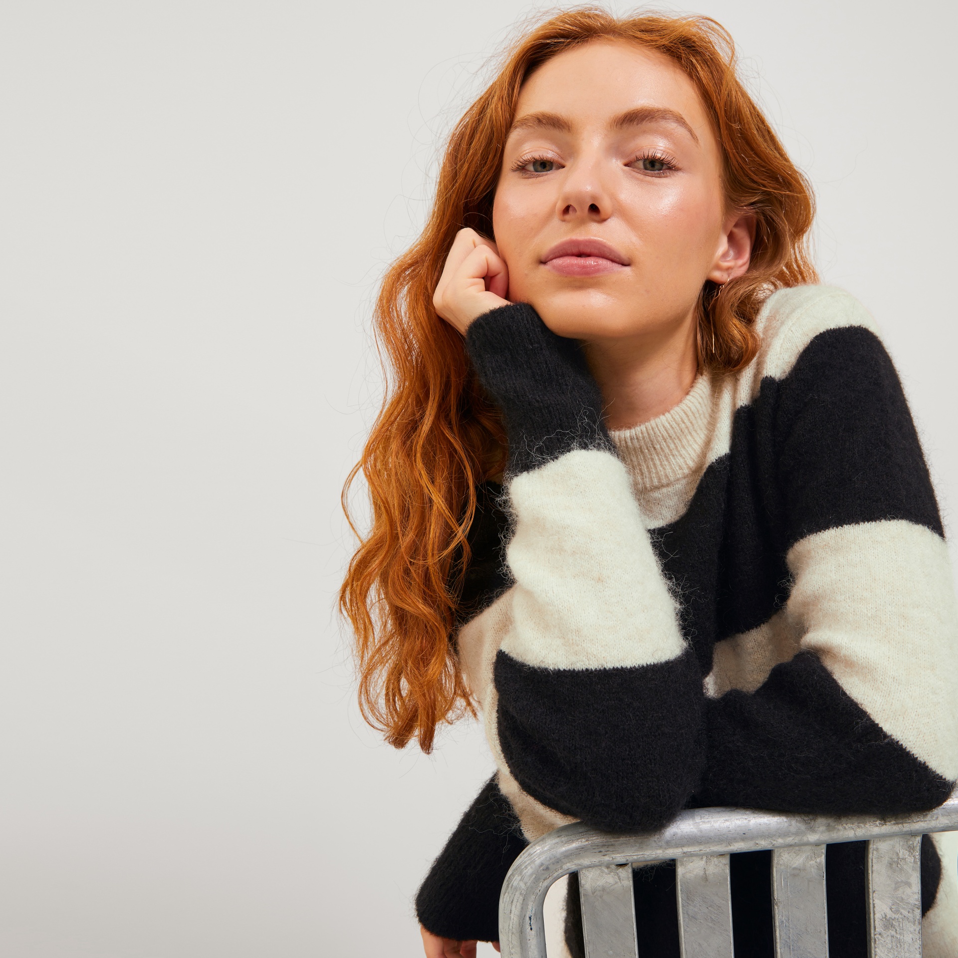Mulher com camisola de riscas em preto e branco apoiada numa cadeira metálica