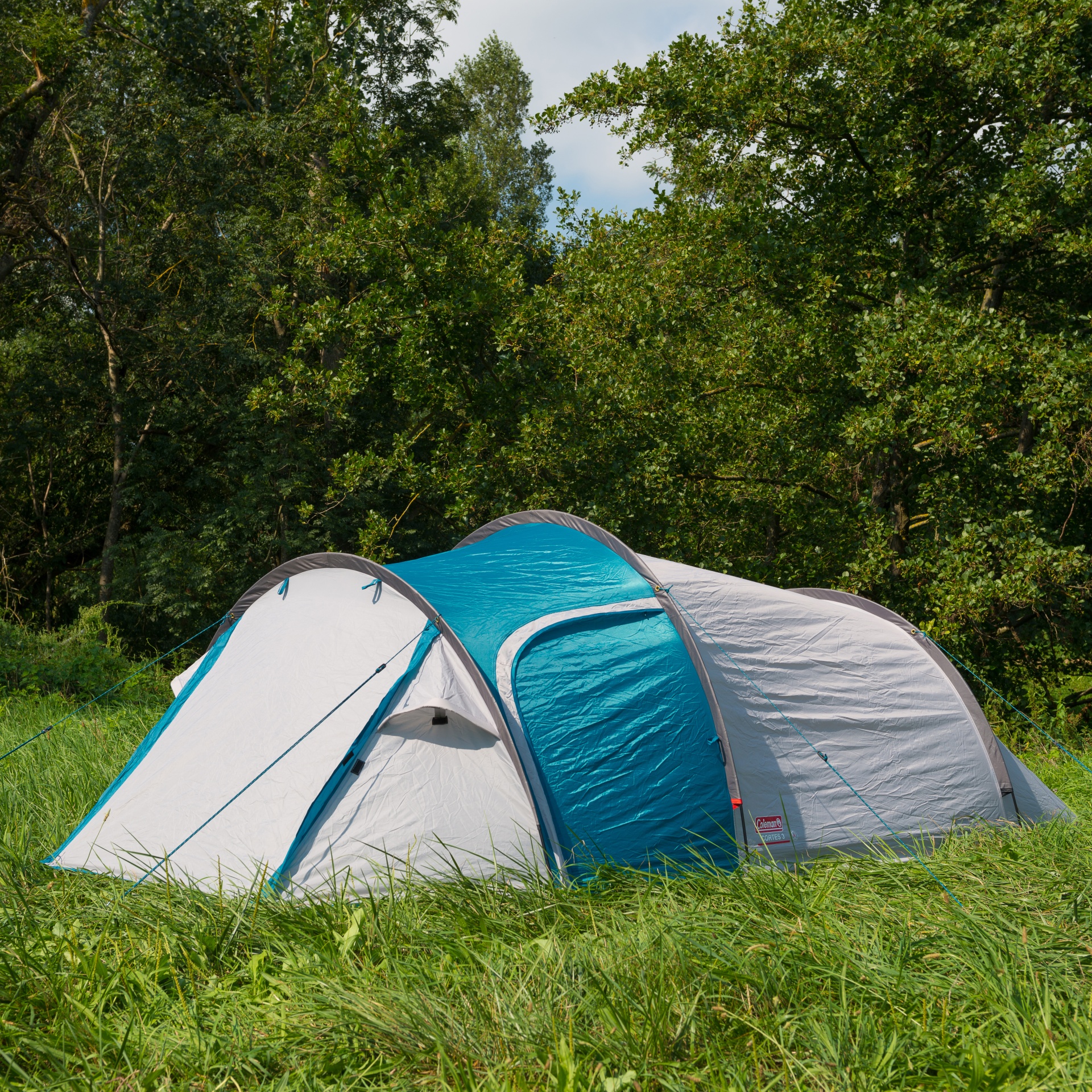 Tenda de campismo Coleman cinzenta e azul em relva com árvores ao fundo