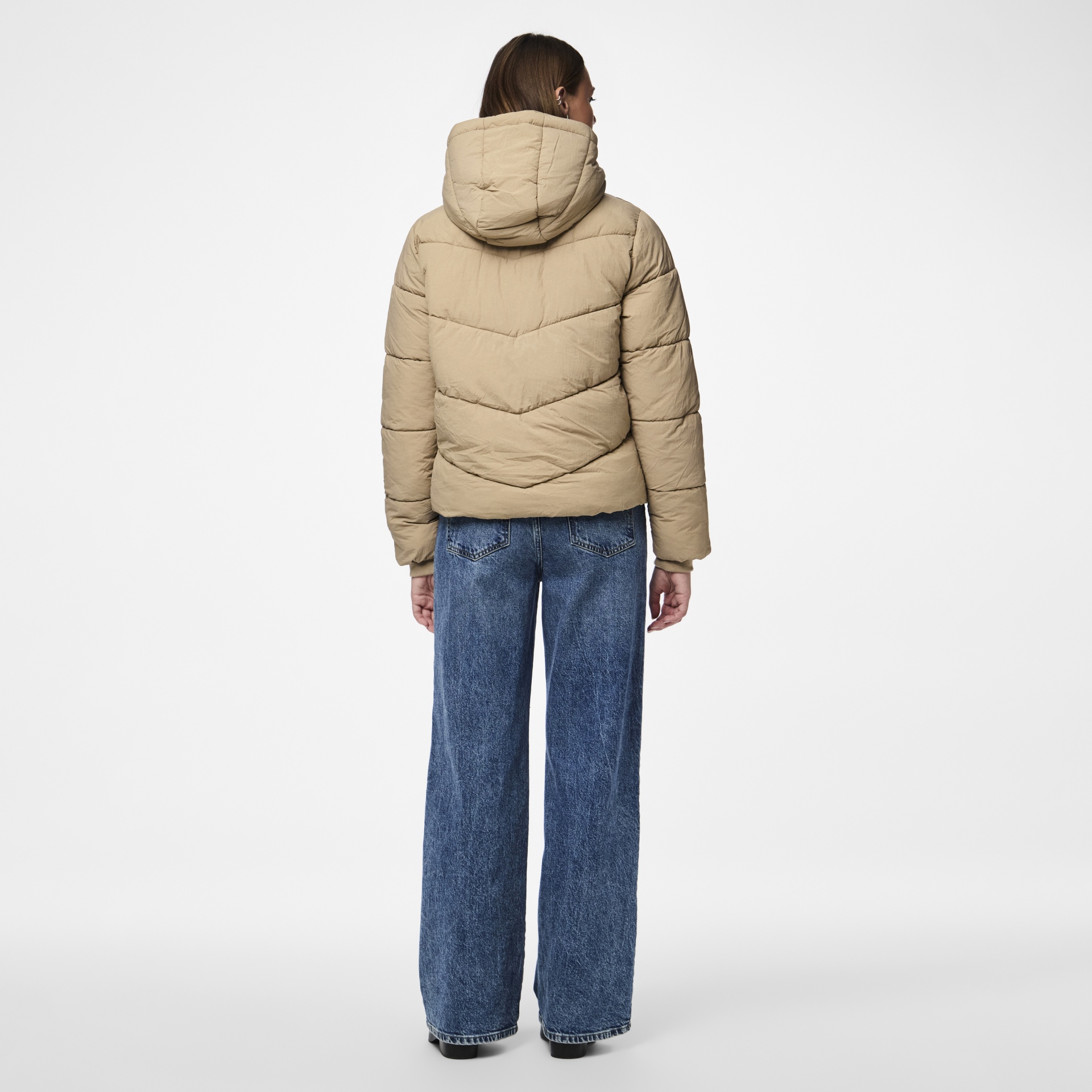 Casaco acolchoado bege com capuz visto de costas, calças de ganga largas azuis.