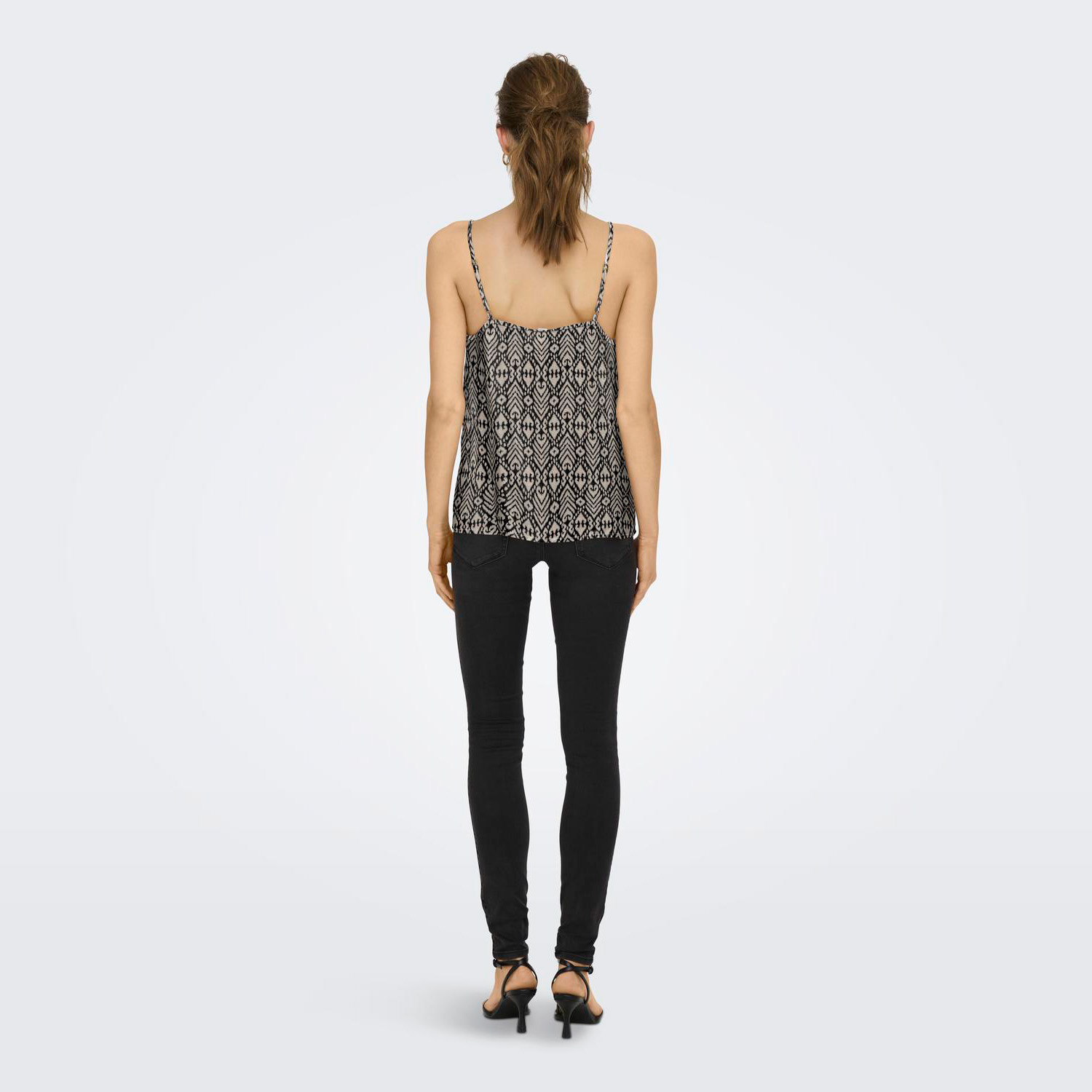 Top feminino preto e branco com padrão geométrico, calças pretas justas e sandálias de salto vistas de costas.