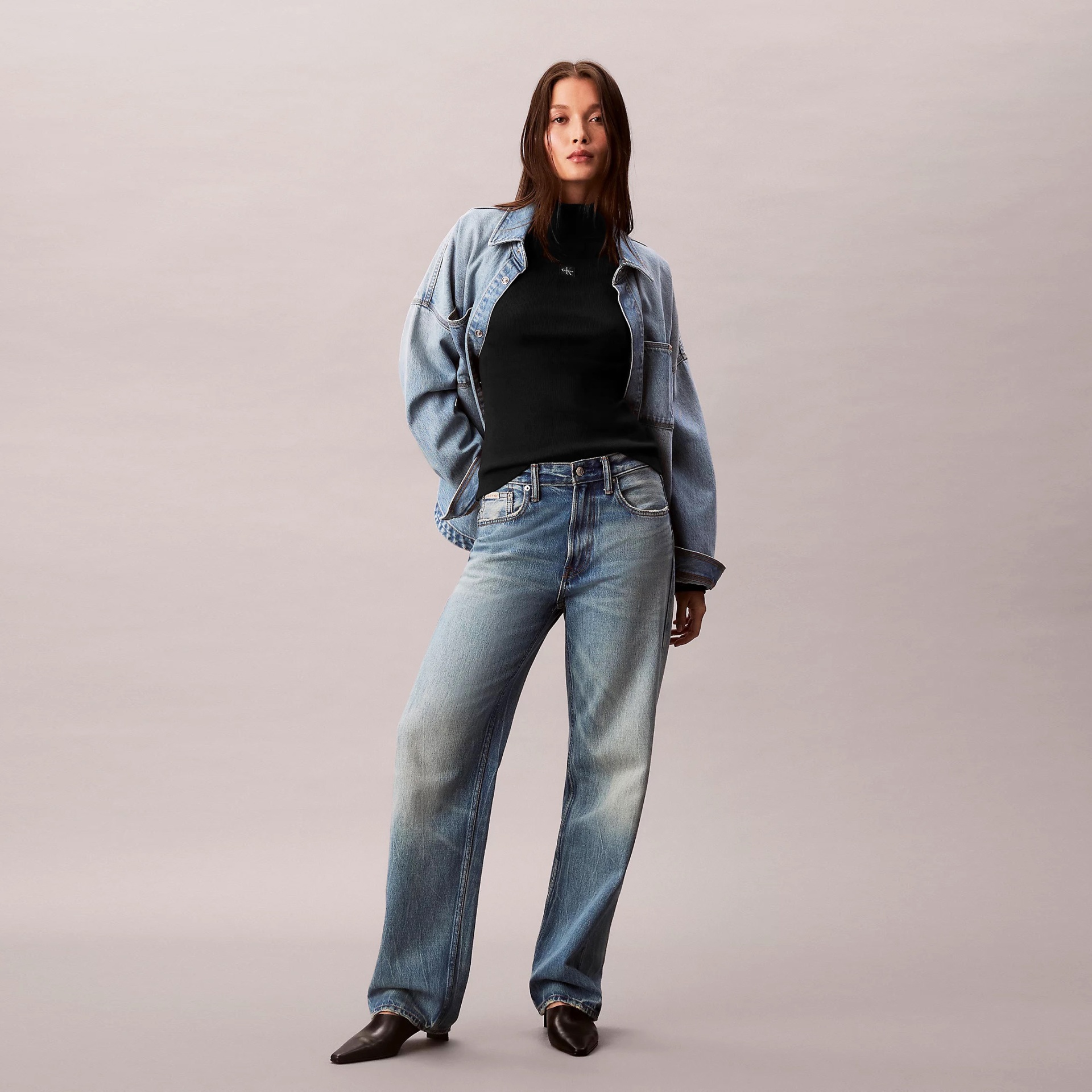 Mulher com casaco, camisola e calças de ganga azuis e sapatos castanhos.