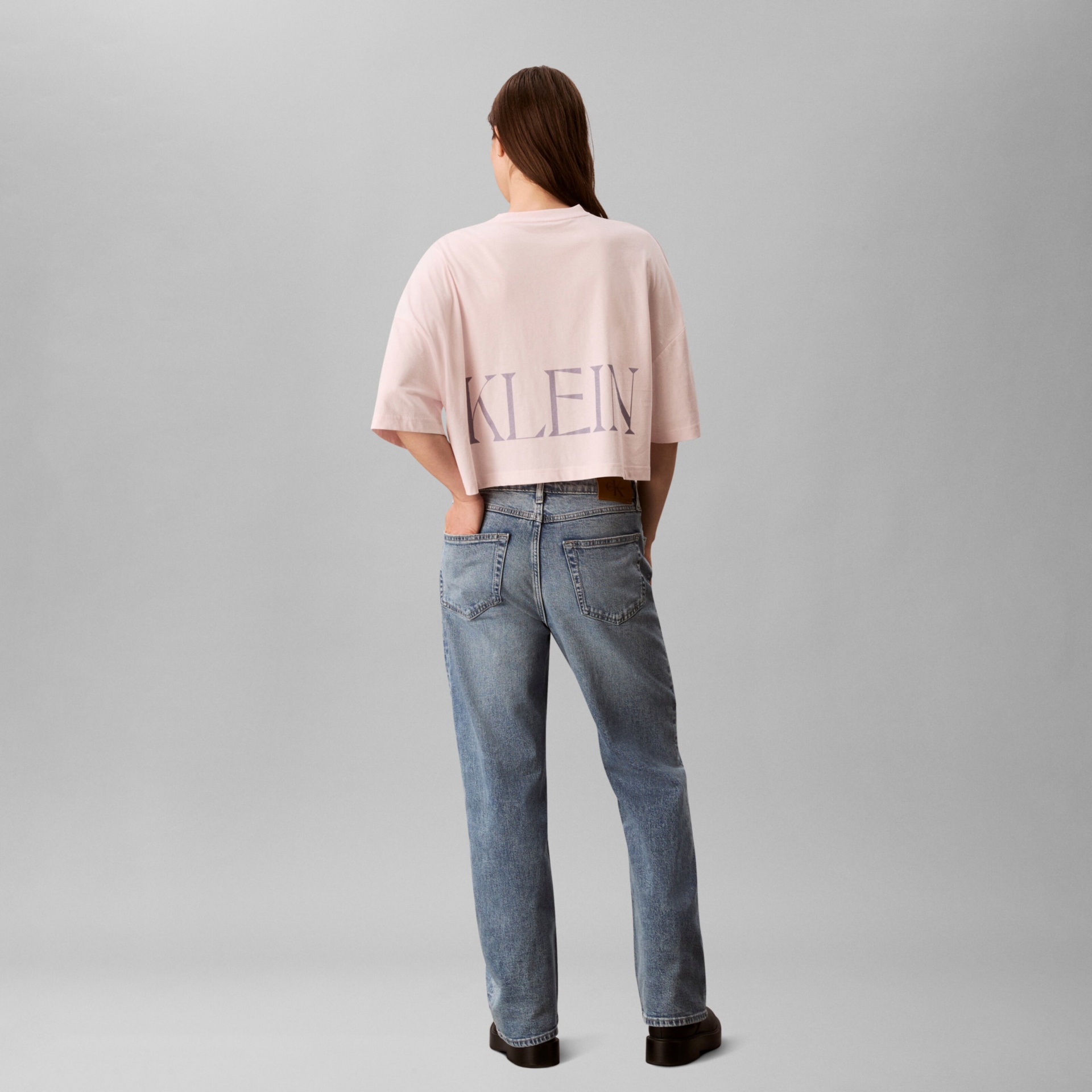 Mulher de costas com camisola rosa curta e jeans azuis