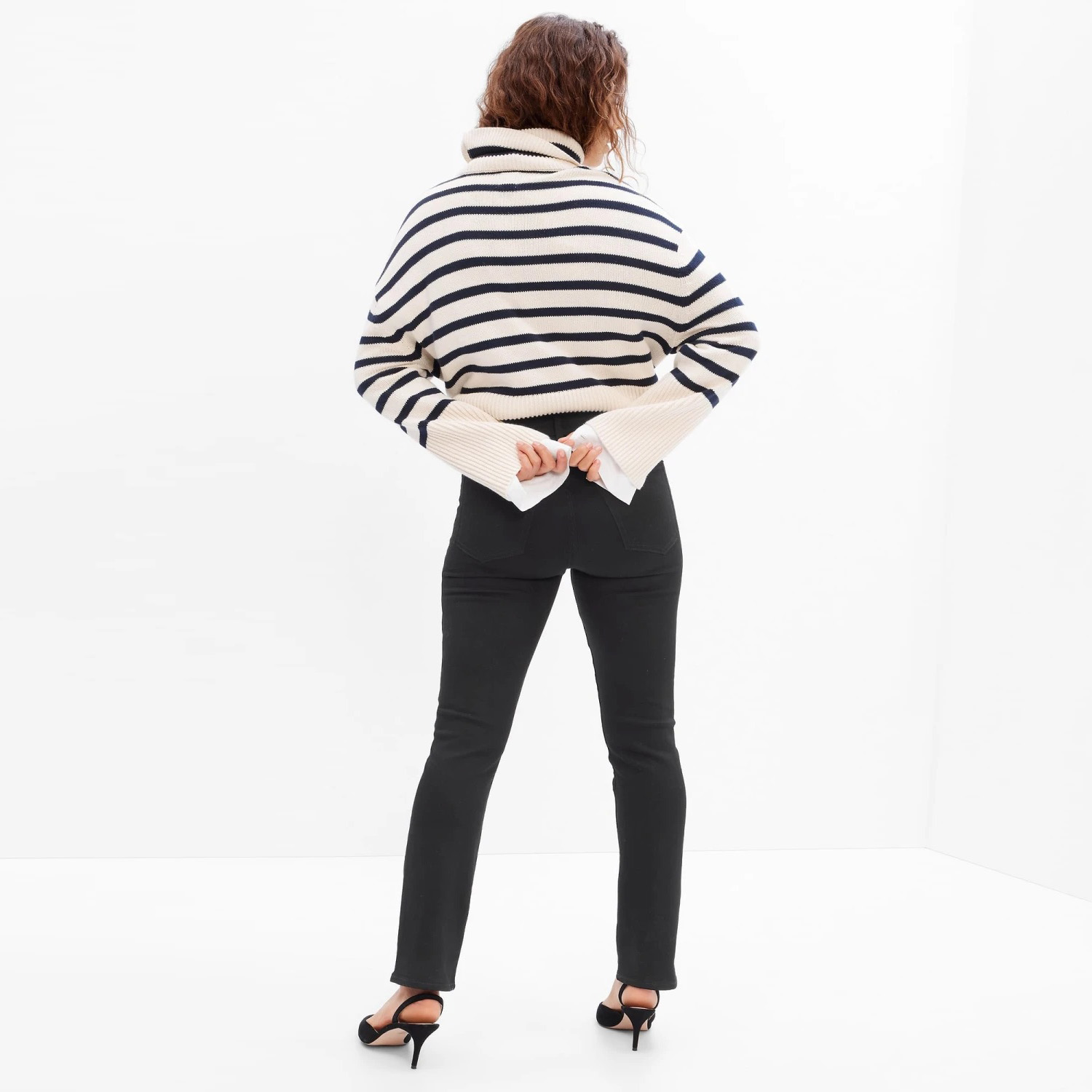 Mulher de costas com camisola às riscas preta e branca, calças pretas e sandálias de tacão preto.