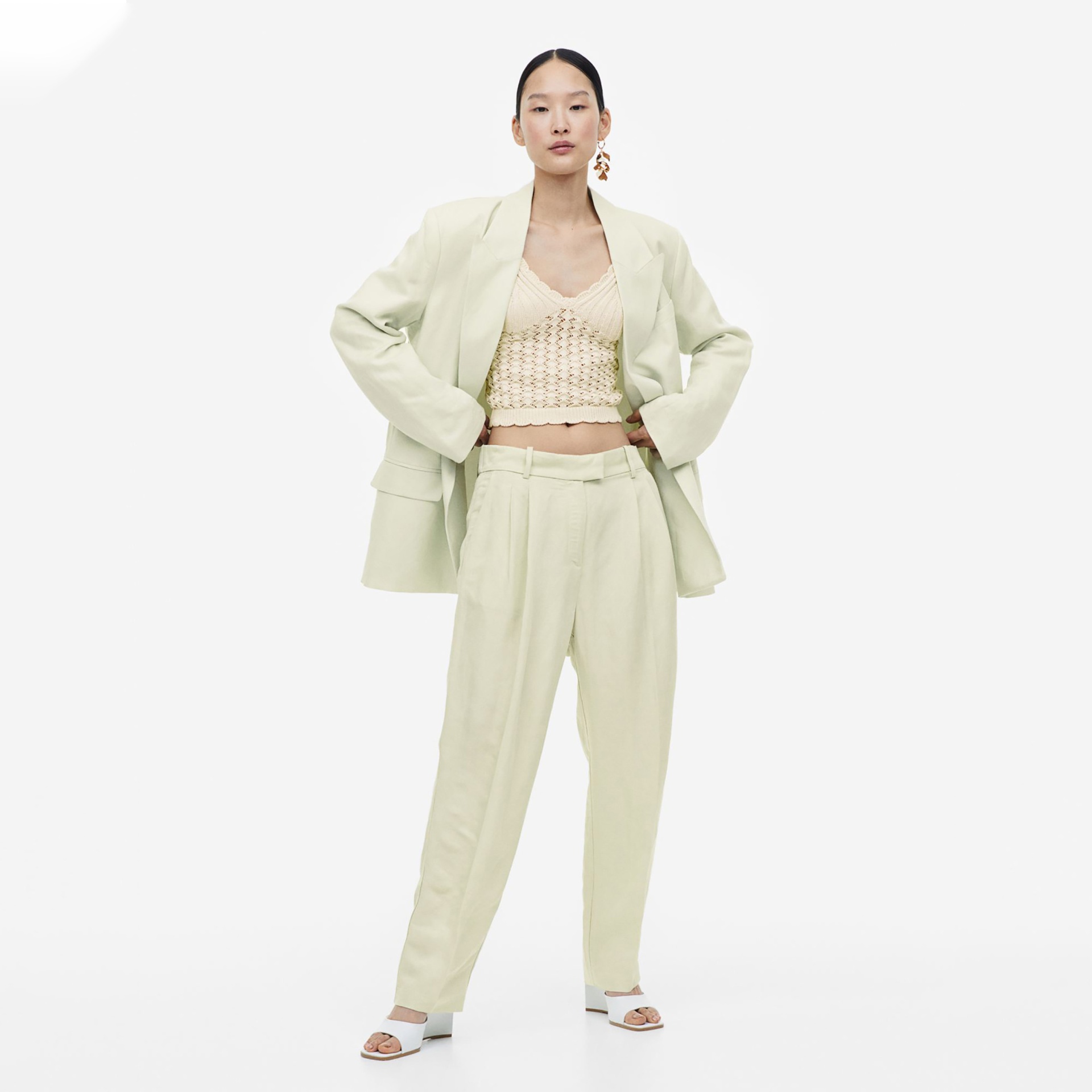 Mulher com blazer e calças salmão claro, top de malha bege claro e sandálias brancas.