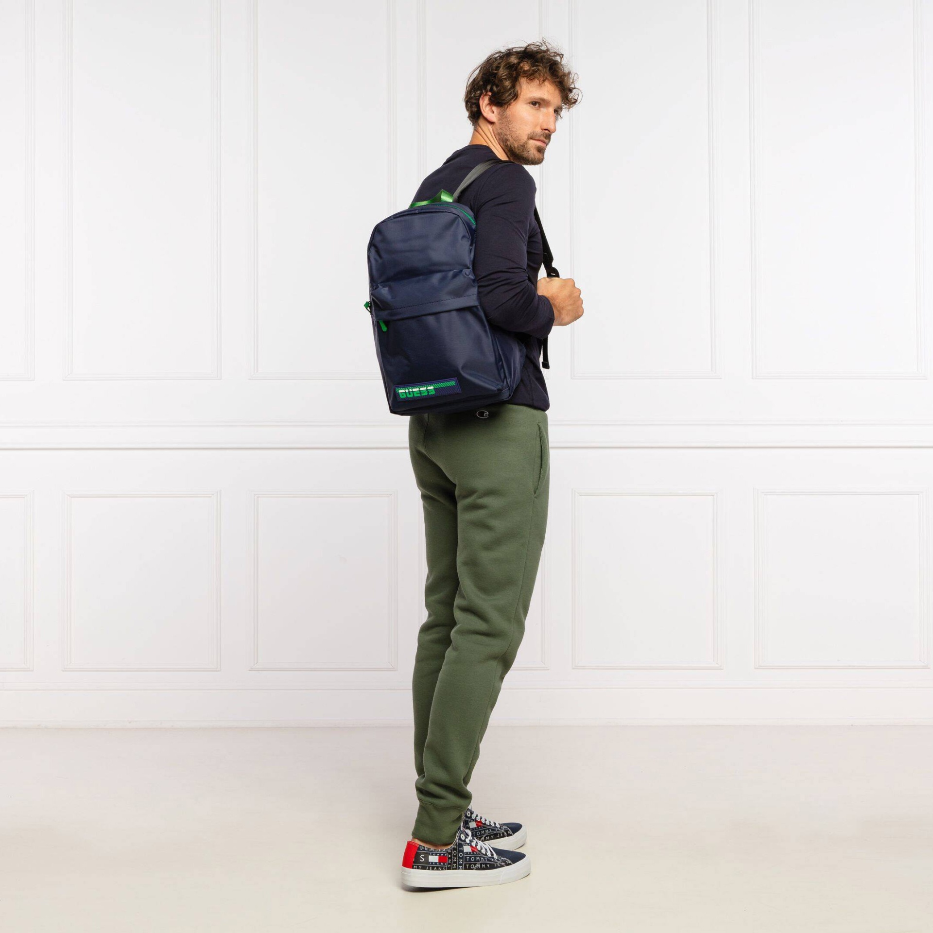 Homem com mochila azul escura com detalhes verdes e calças verdes de ganga