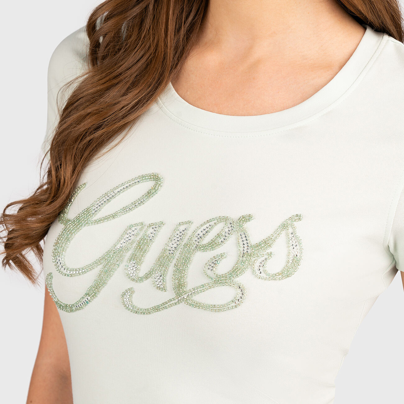 T-shirt branca com a palavra Guess em strass verde claro e transparente