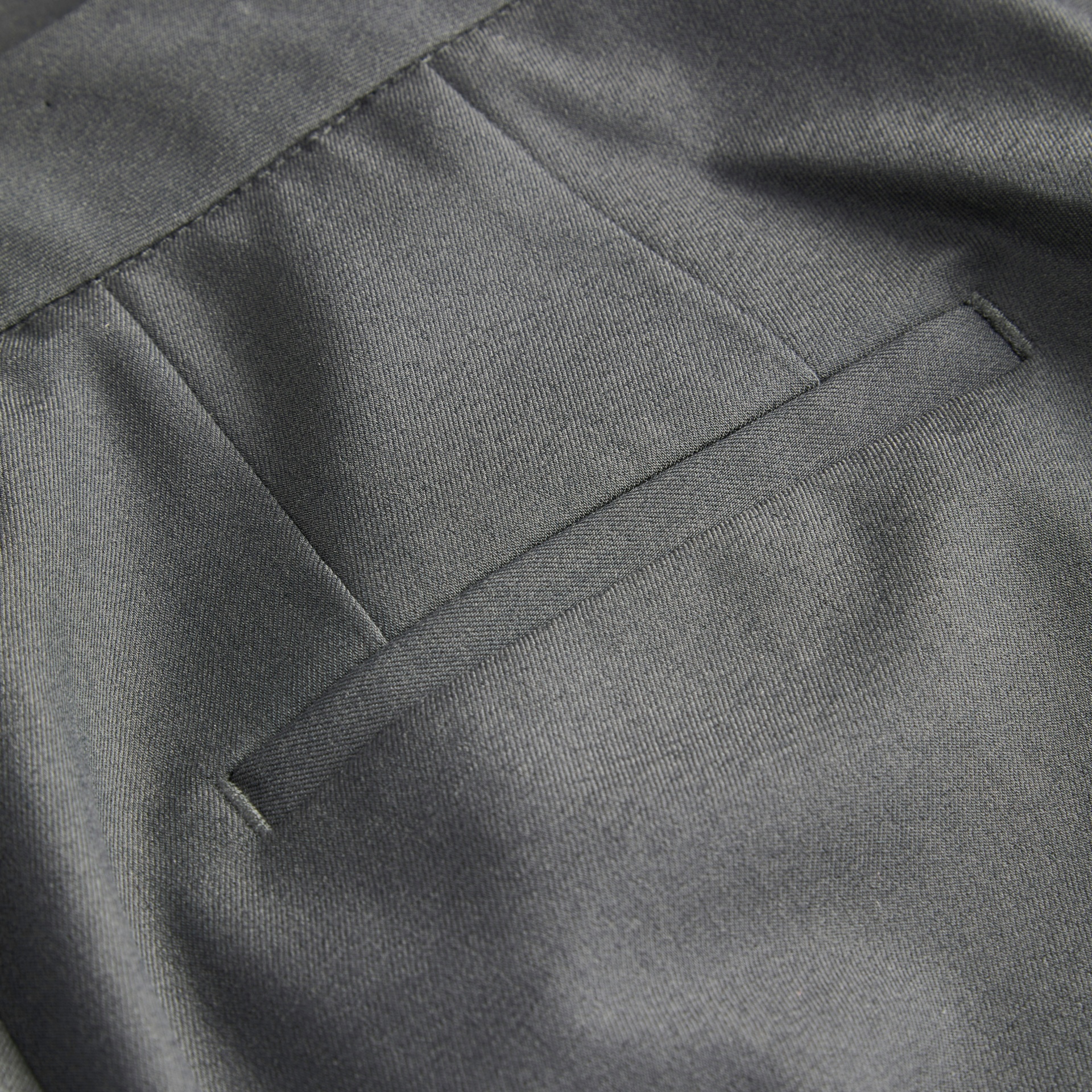 Pormenor de bolso traseiro de calças cinzentas de tecido liso
