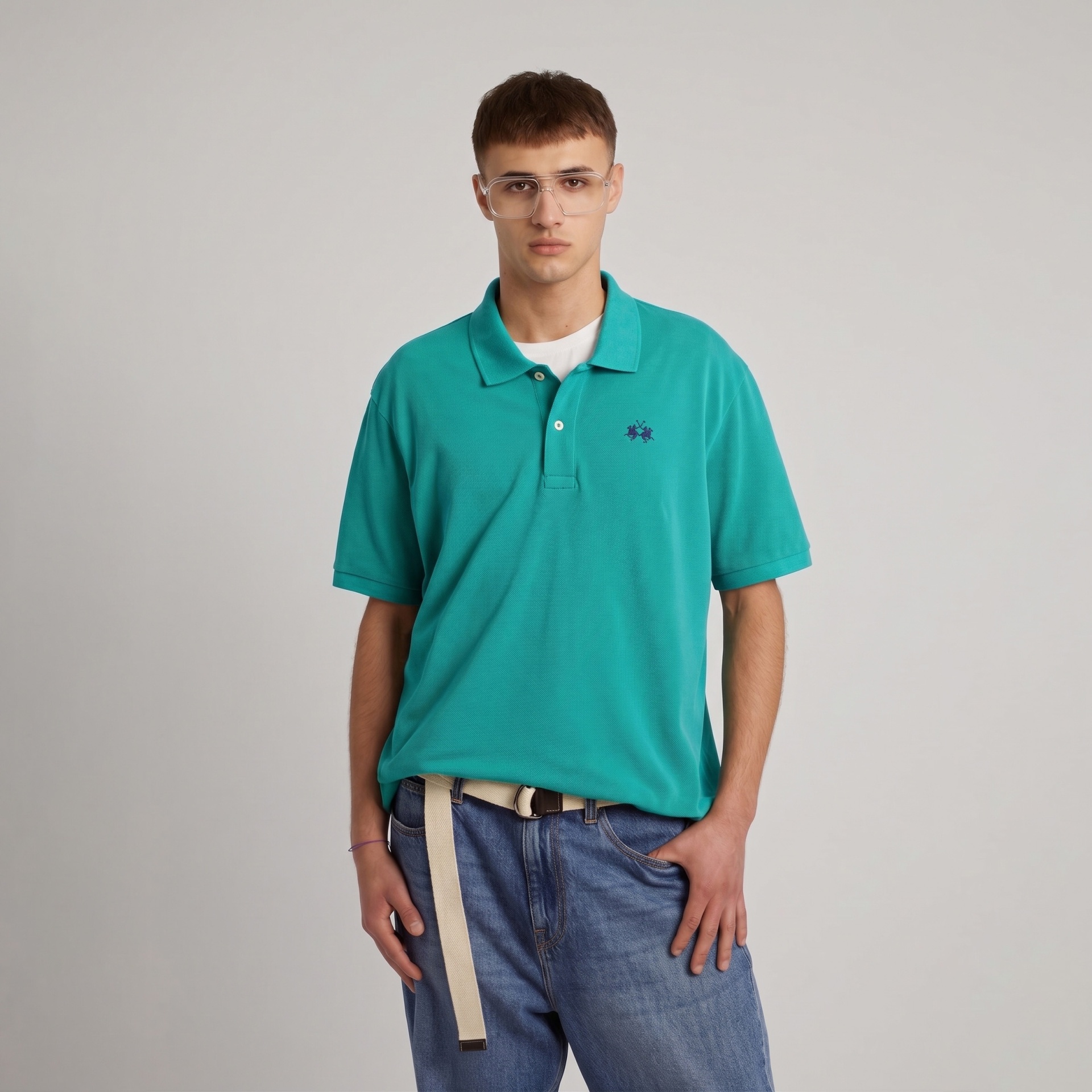 Homem com camisa polo verde água, óculos grandes, jeans azul claro e cinto branco.