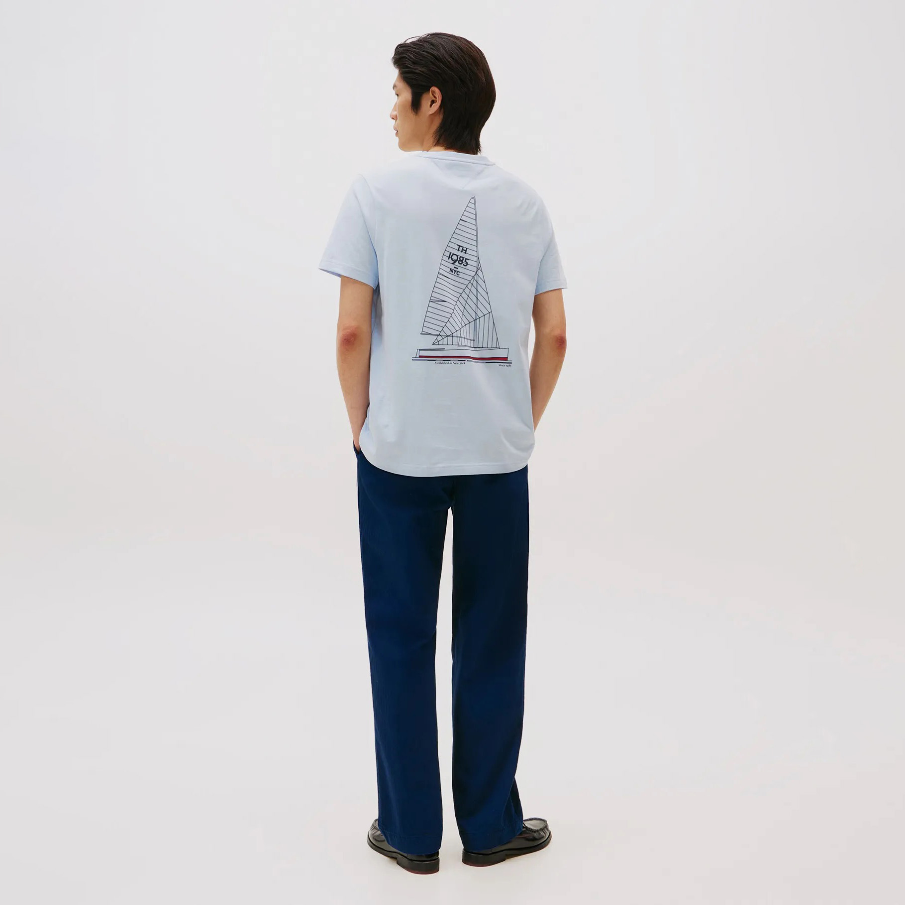 Camiseta azul claro com estampa de veleiro nas costas vista de trás, combinada com calças azul-escuras