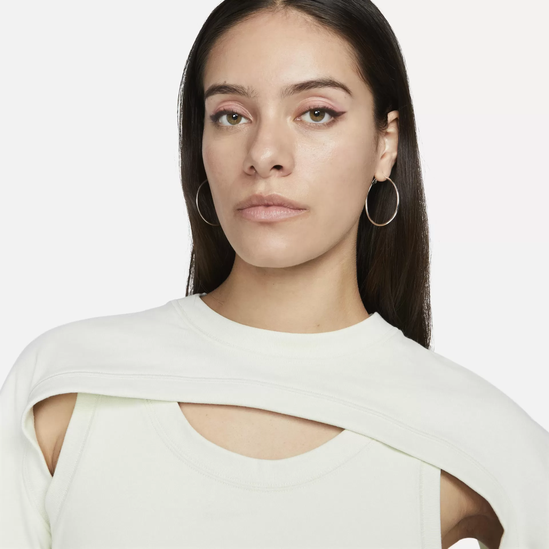 Mulher com brinco de argola dourado e camiseta branca com recorte