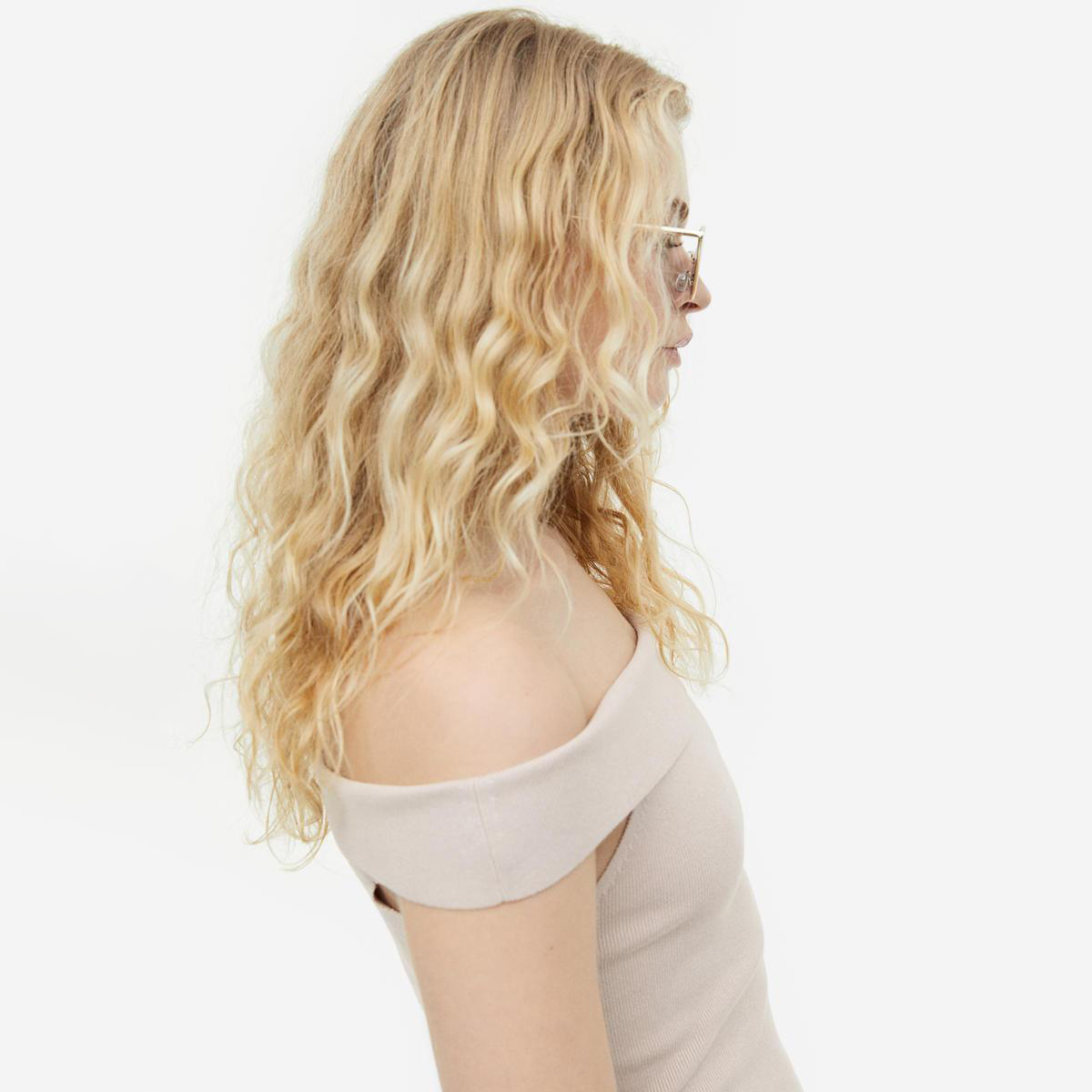 Mulher com t-shirt bege de ombros descobertos e óculos, vista de perfil