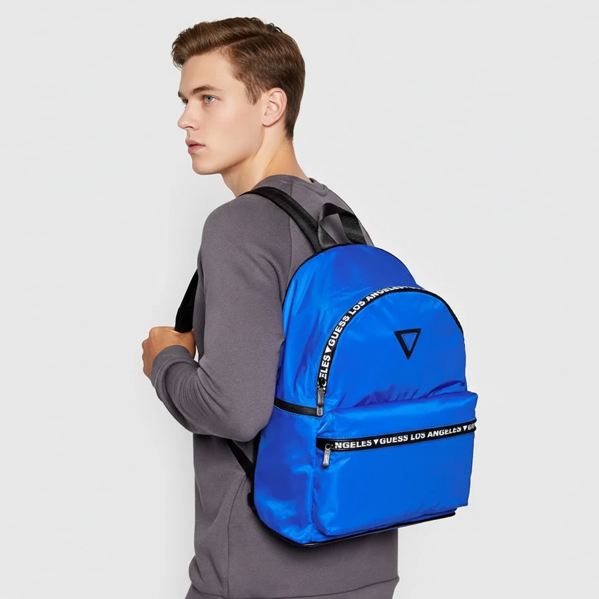 Homem de lado com mochila azul Guess e camisola cinza