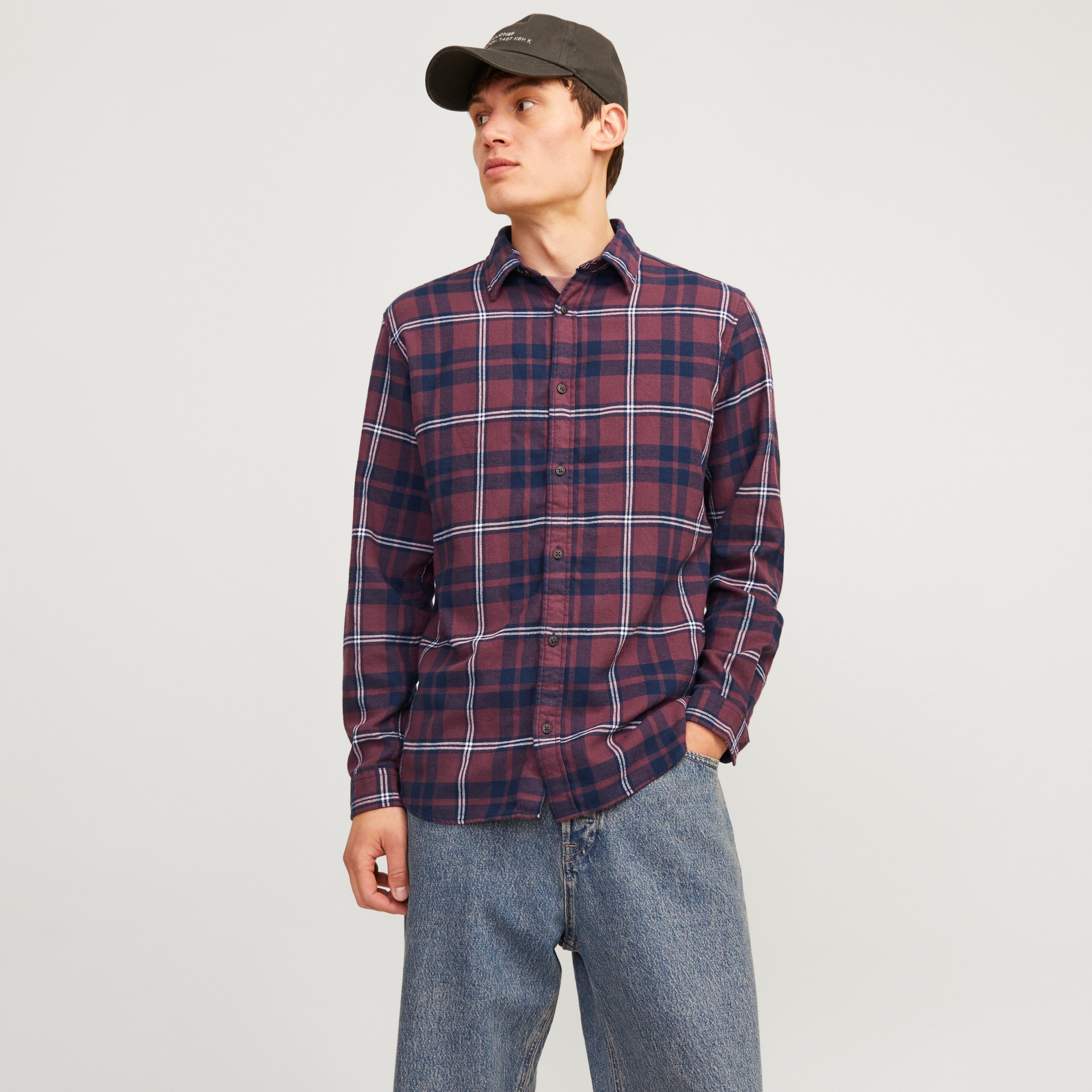 Camisa de manga comprida xadrez vermelha, azul e branca usada por homem com calças de ganga e boné