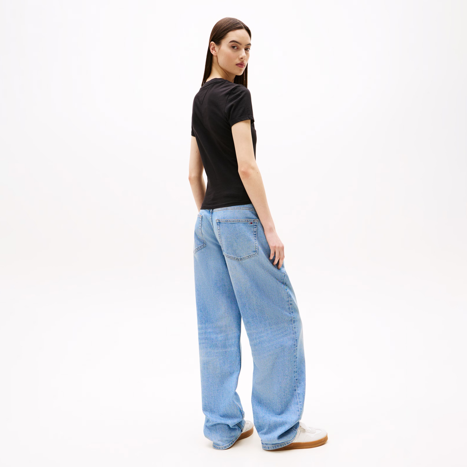 Mulher com t-shirt preta e jeans azuis largos em fundo branco