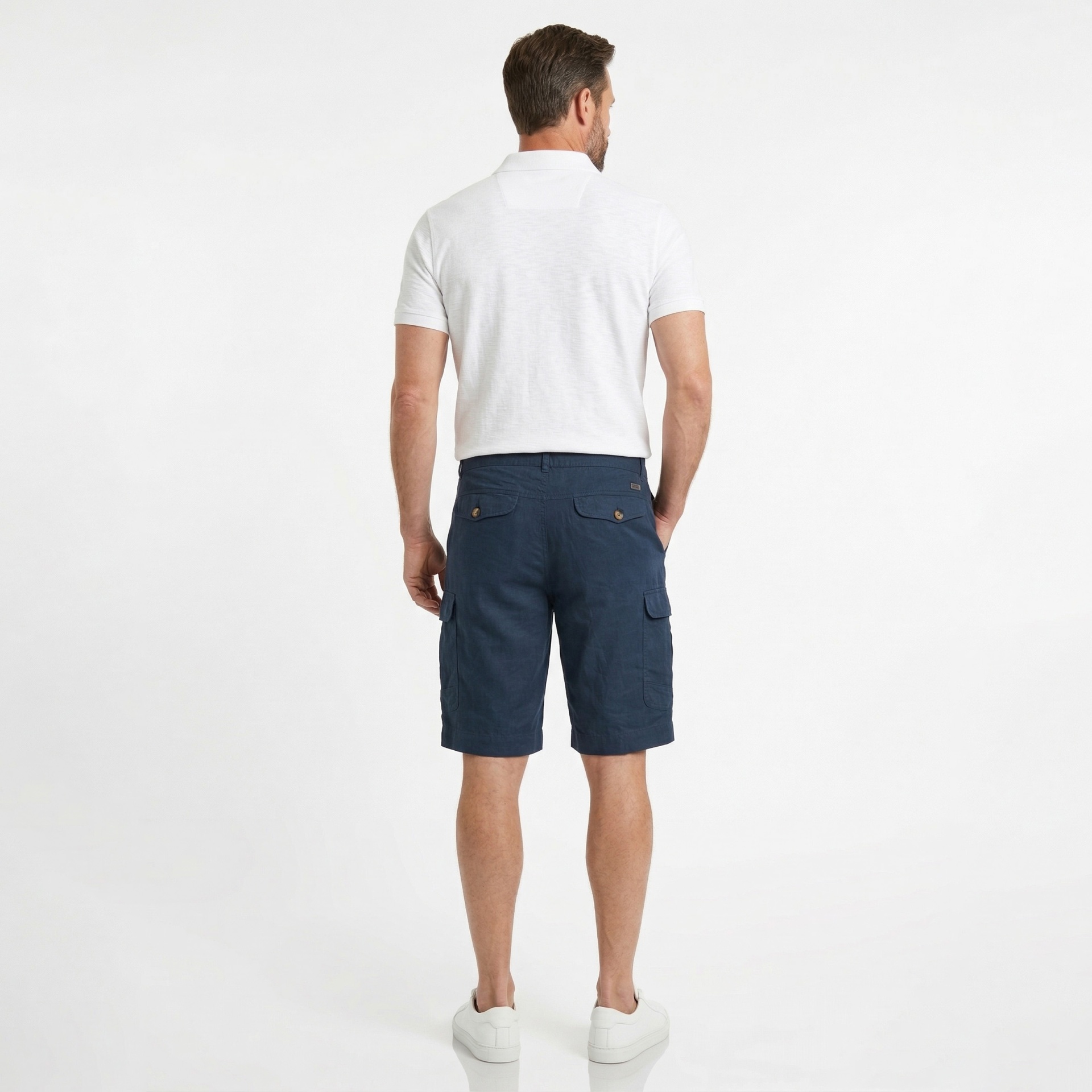 Homem de costas com t-shirt branca, calções cargo azuis escuros e sapatilhas brancas.