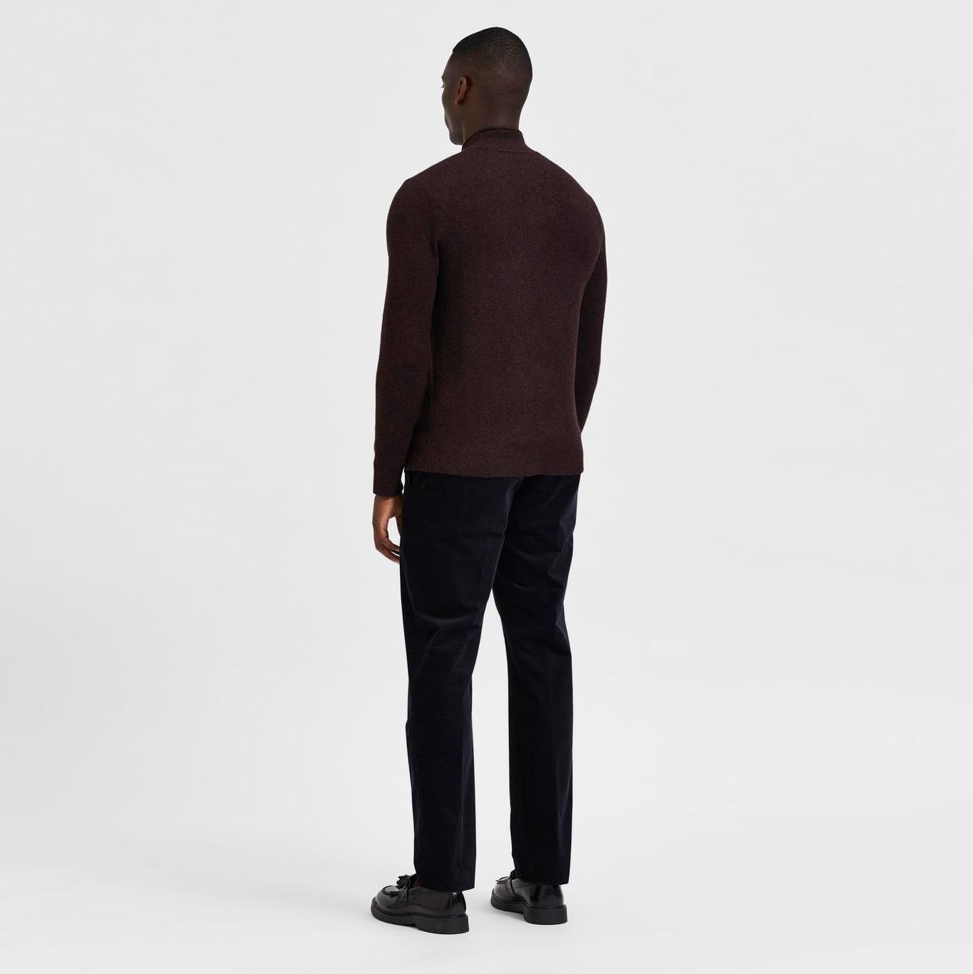 homem veste camisola castanha de gola alta, calças pretas e sapatos pretos, visto de costas