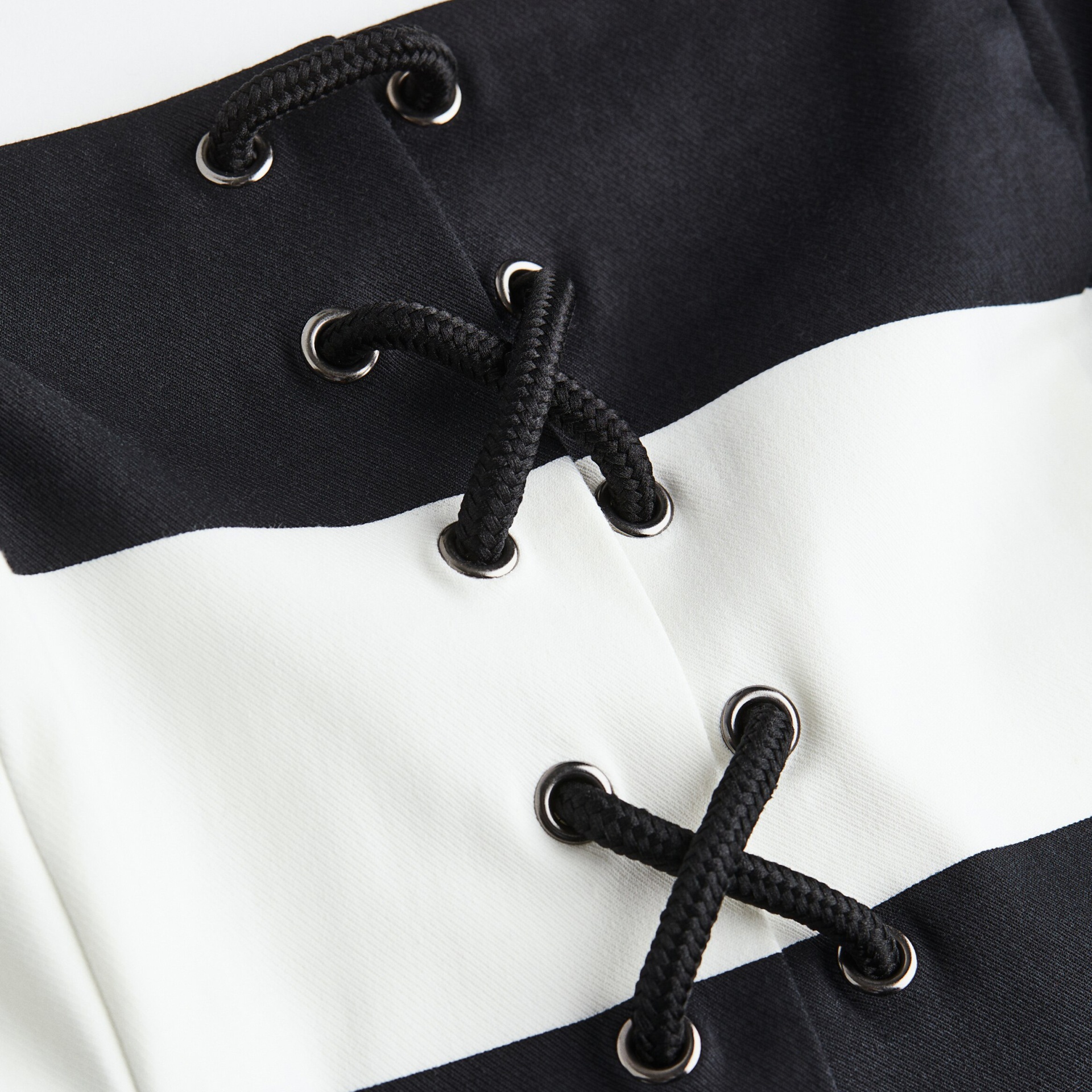 Pormenor de peça de roupa preta e branca com cadarço preto e ilhóses metálicos