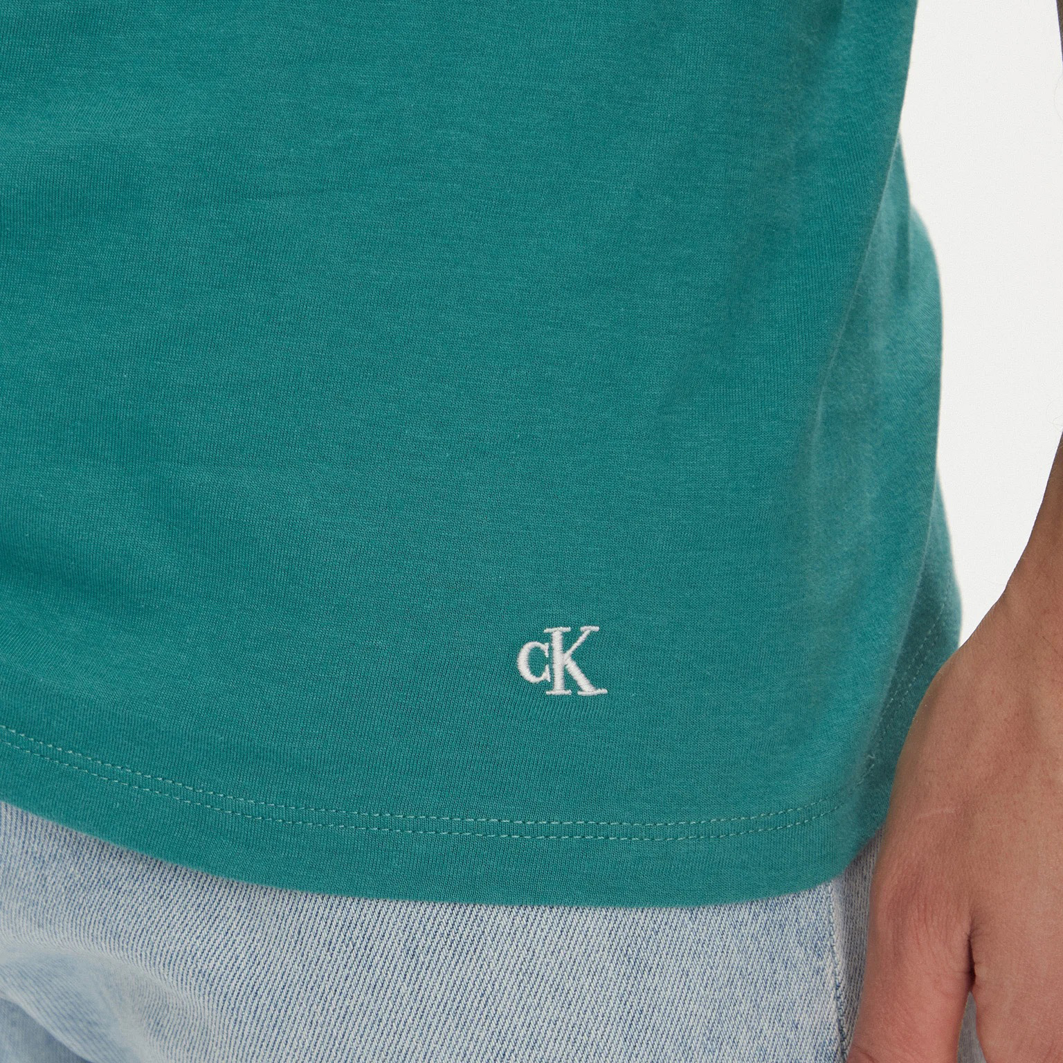 Detalhe de t-shirt verde com bordado cK e jeans azul claro