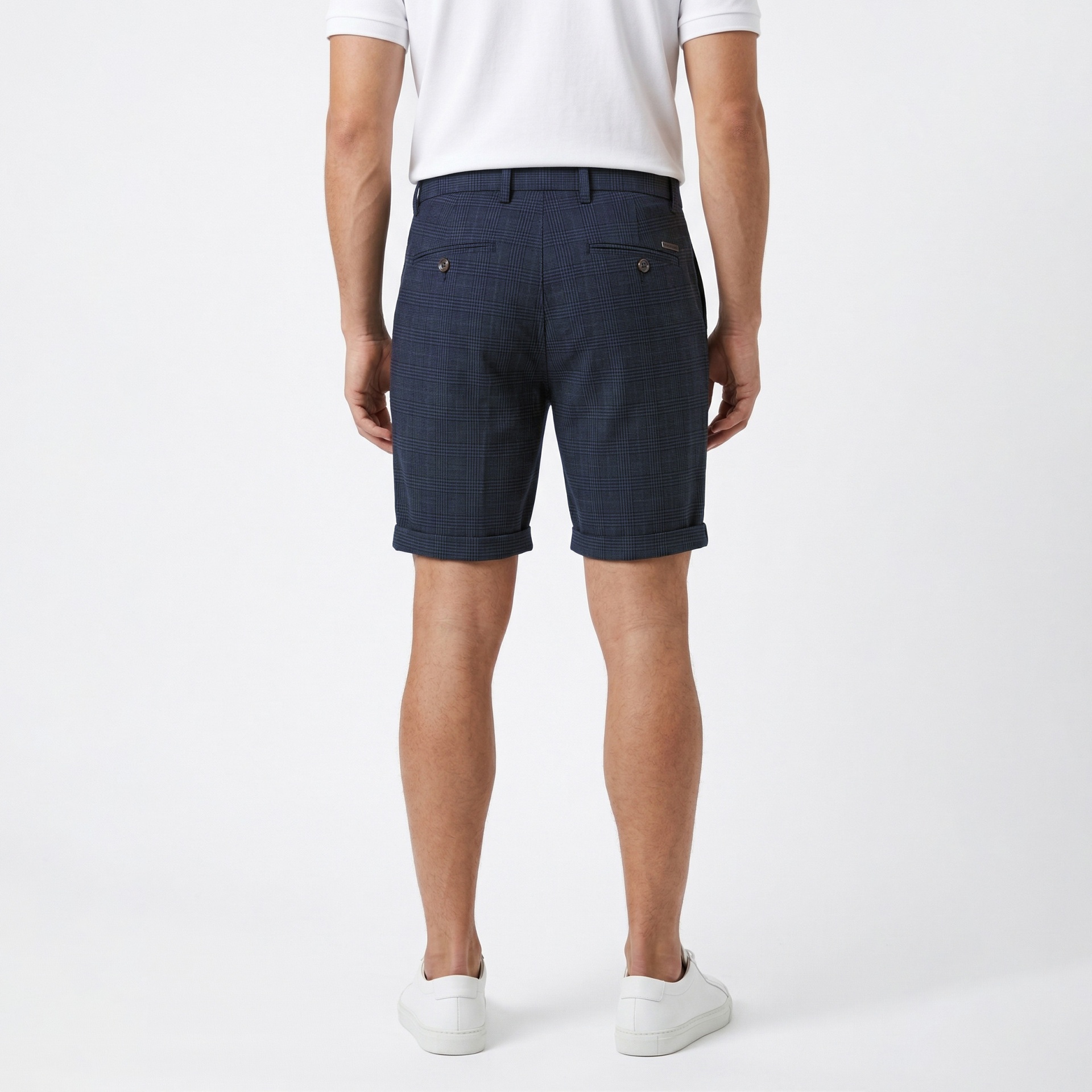 Calções azuis escuros com padrão xadrez vistos de trás numa pessoa com camiseta branca e sapatos brancos