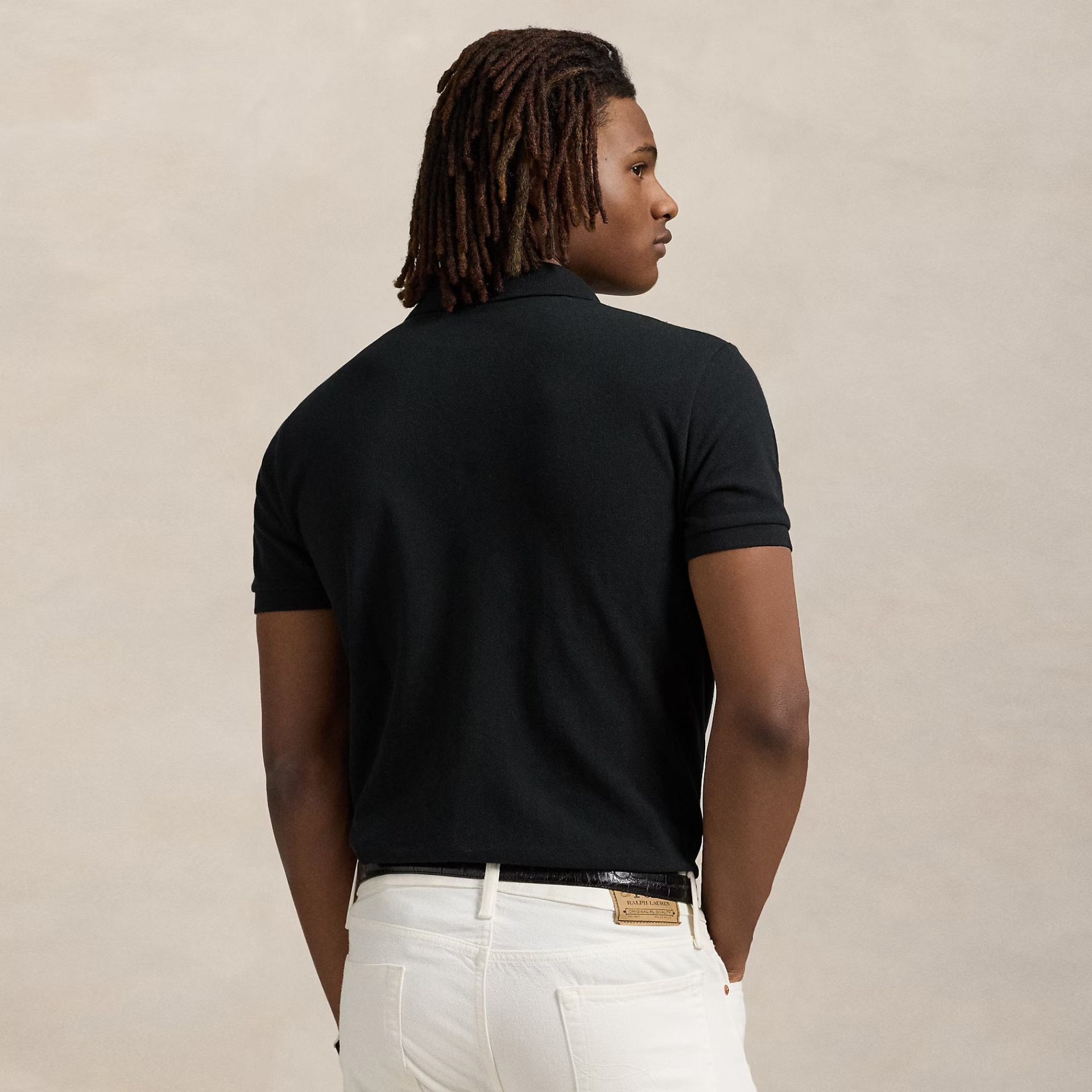 Homem de costas com t-shirt polo preta e calças brancas