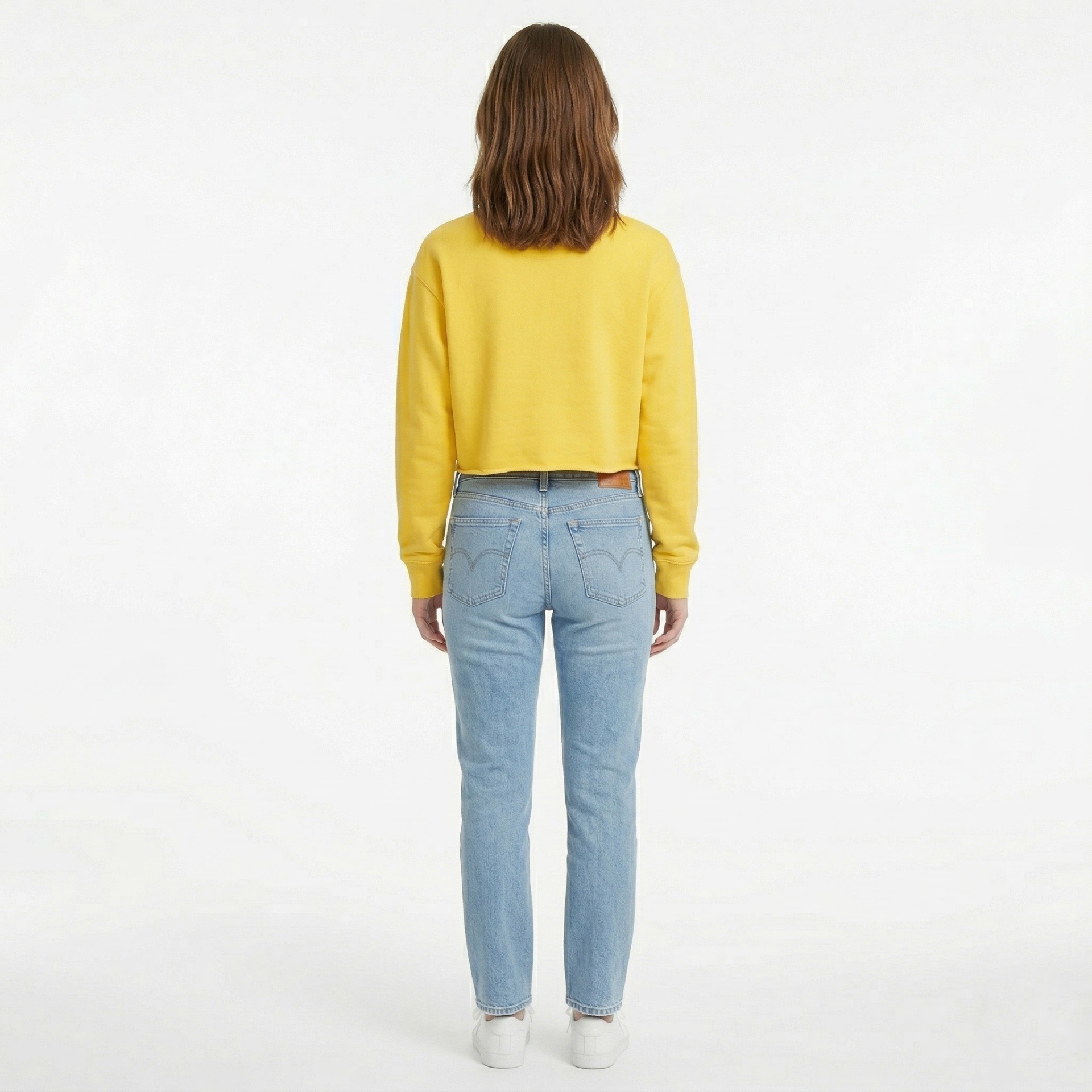 Pessoa de costas com camisola amarela, jeans azuis e ténis brancos