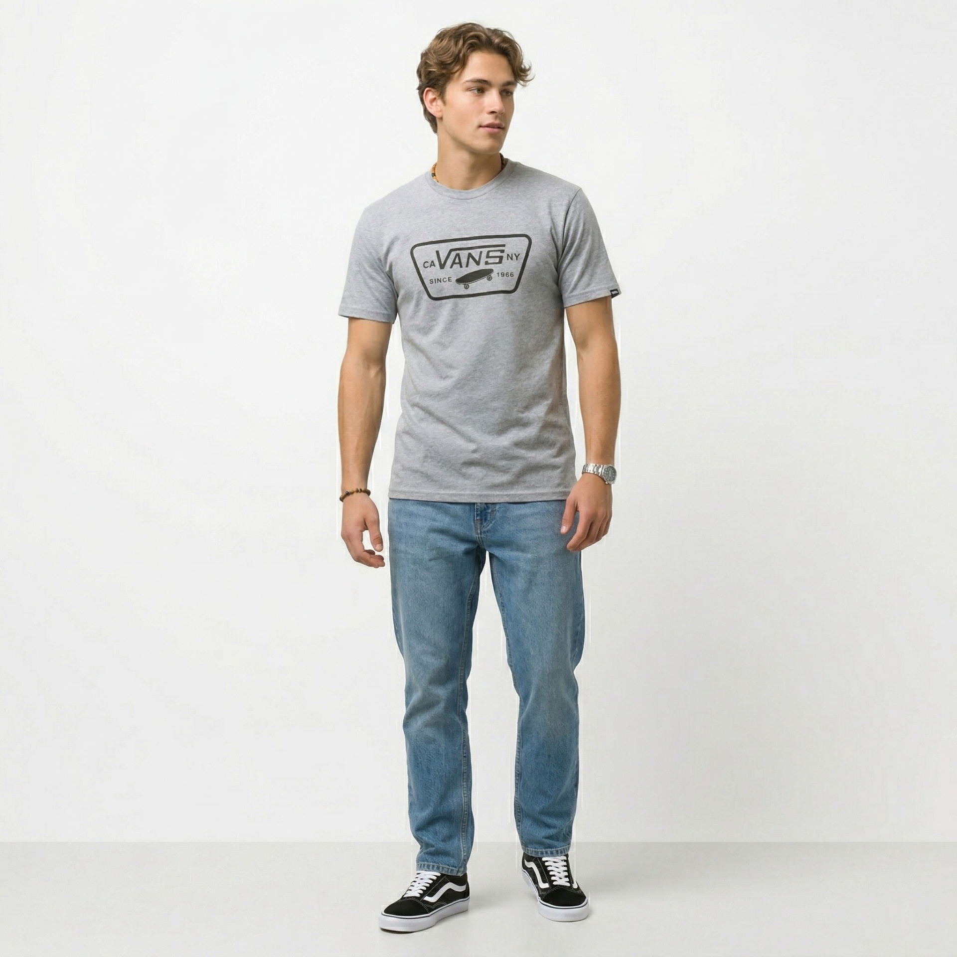 Homem com t-shirt cinzenta VANS, jeans azuis e sapatilhas Vans pretas e brancas