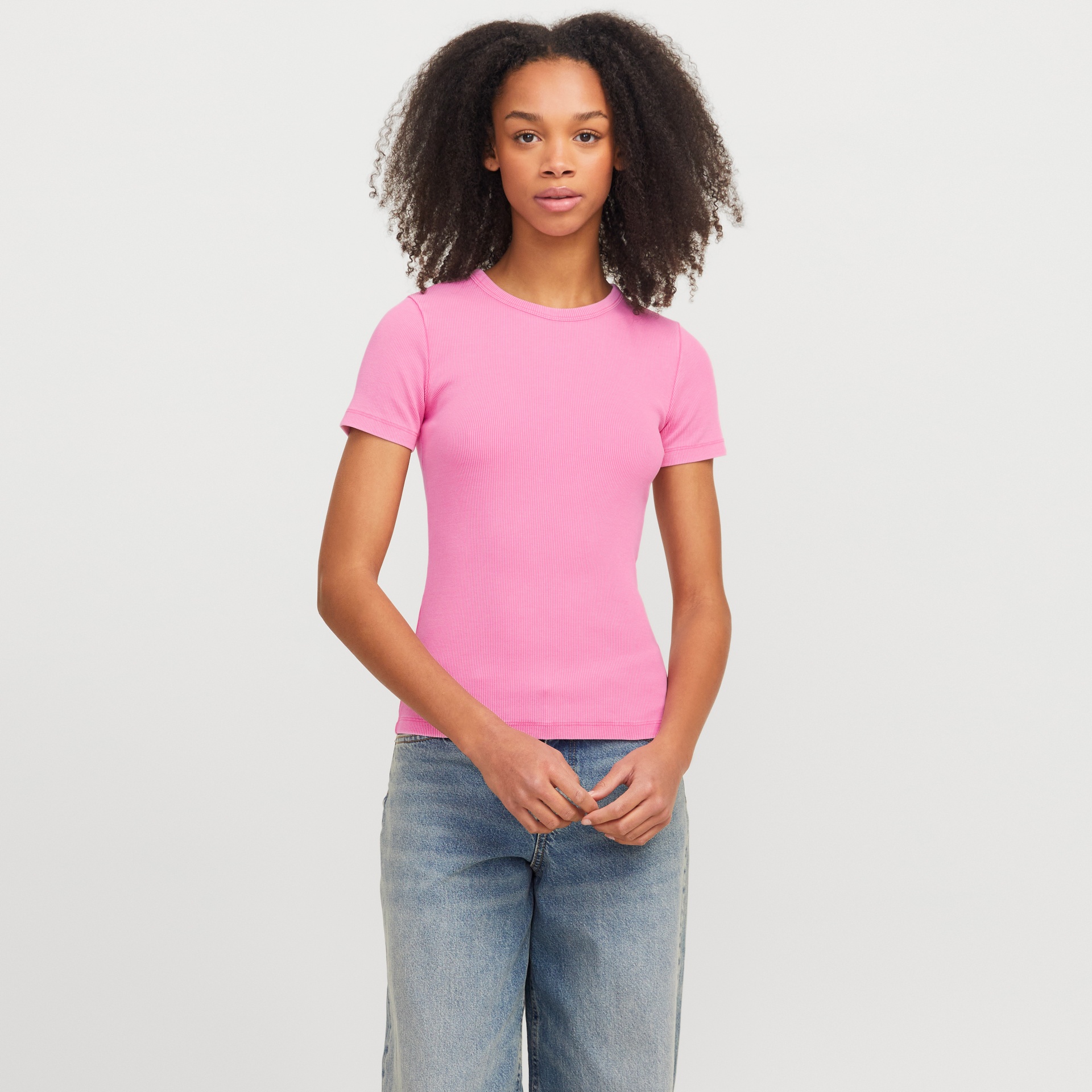 Mulher com t-shirt rosa de malha canelada e calças de ganga azuis claras num fundo branco.