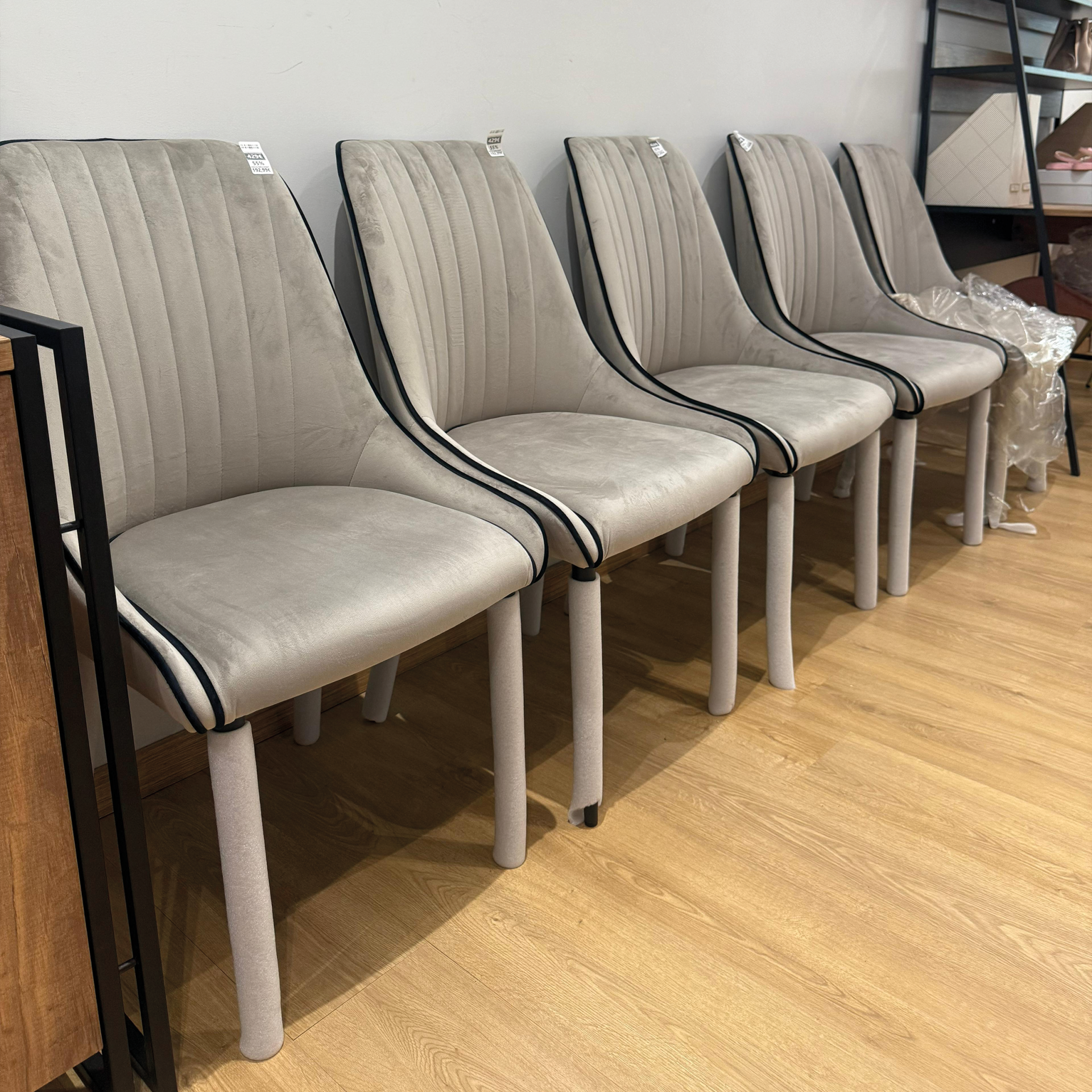 Cinco cadeiras cinza com detalhes pretos e pernas claras alinhadas no chão de madeira