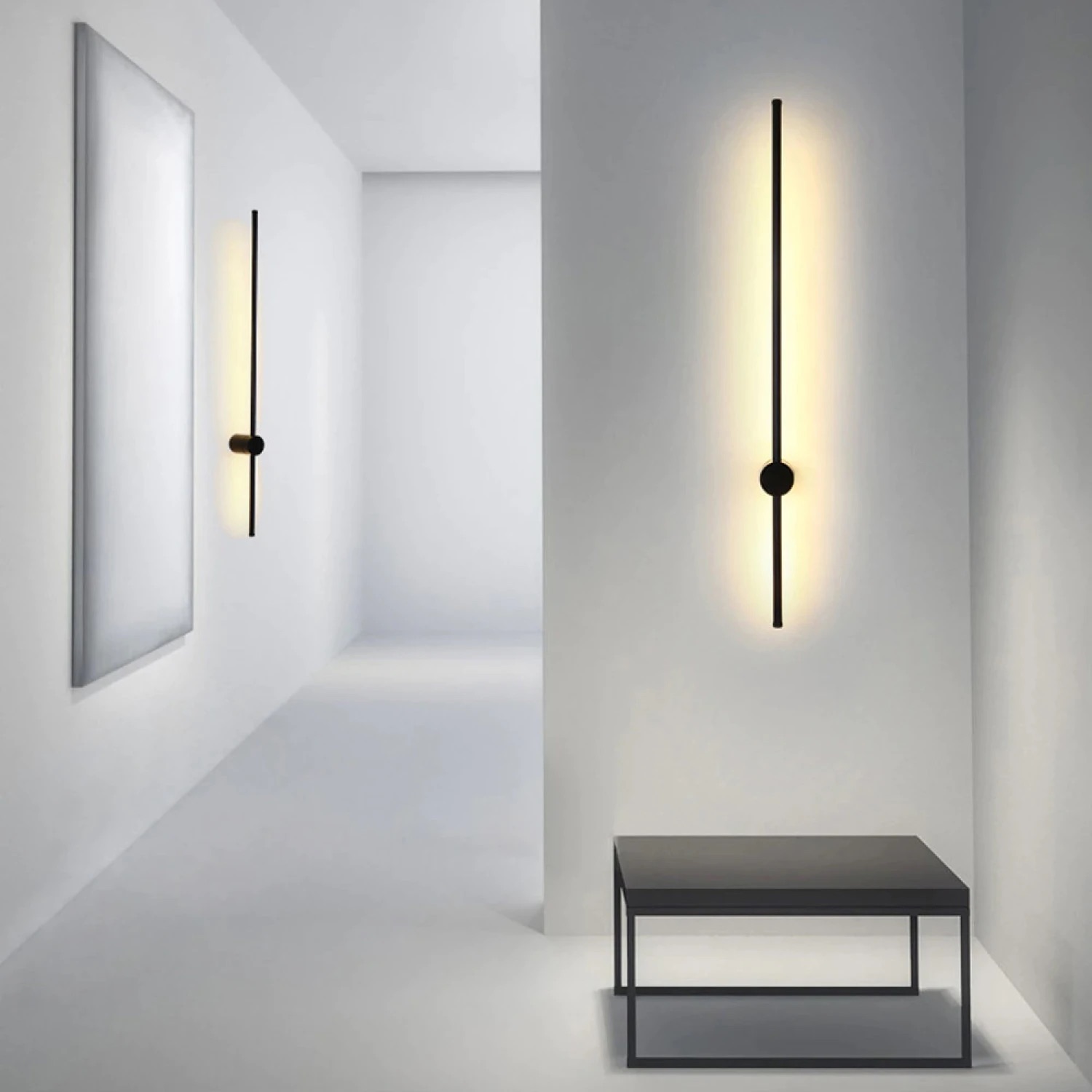 Candeeiro de parede vertical minimalista preto iluminado numa parede branca ao lado de mesa baixa preta