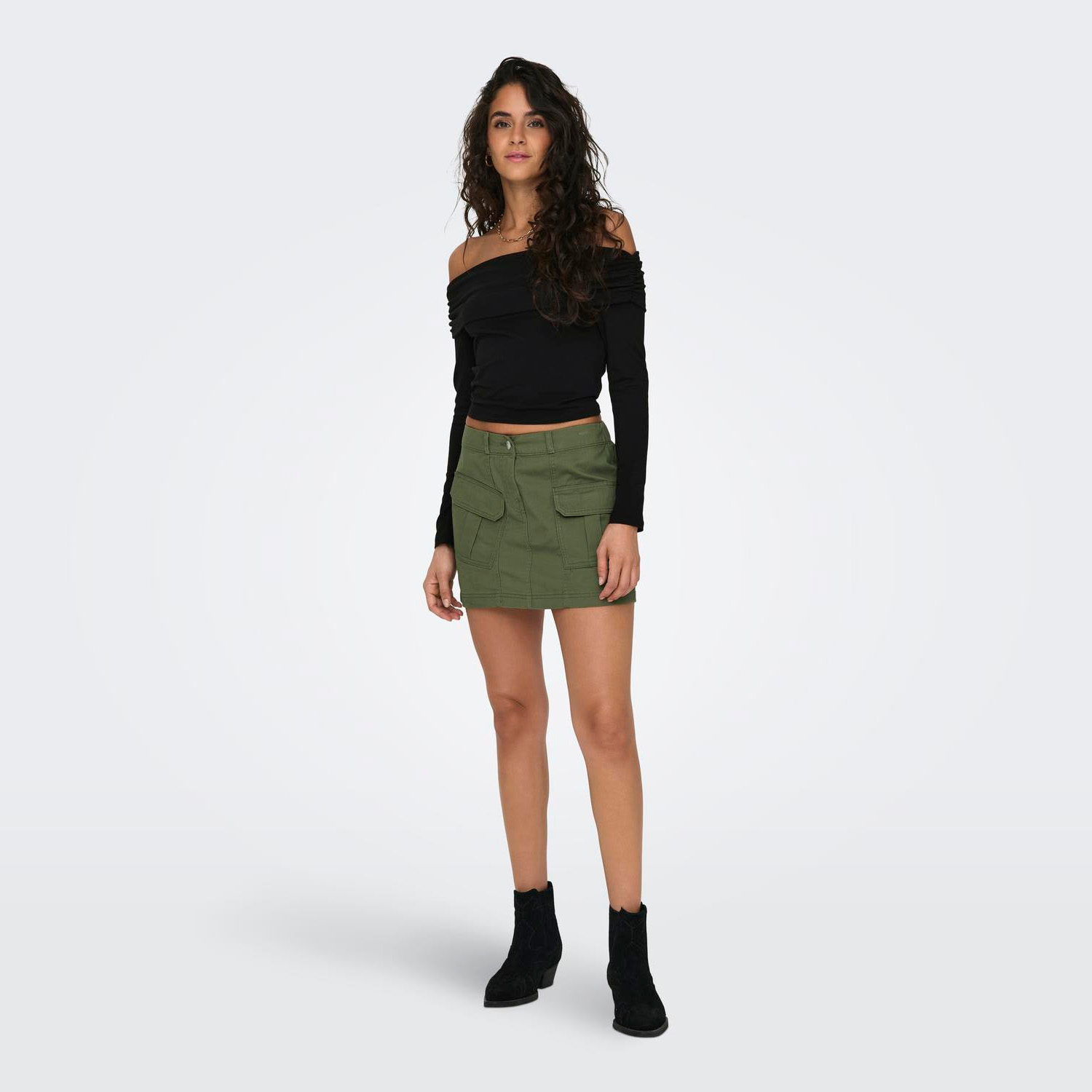 Mulher a usar mini saia verde com bolsos, top preto ombro a ombro e botas pretas.