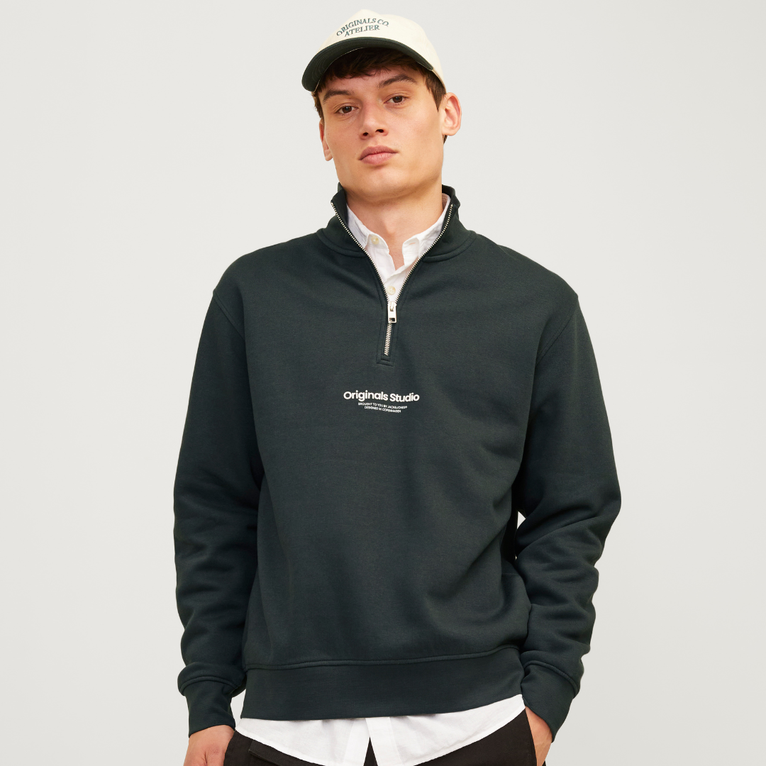 Camisola preta com fecho e logo branco, usada por modelo com camisa branca e boné branco com texto