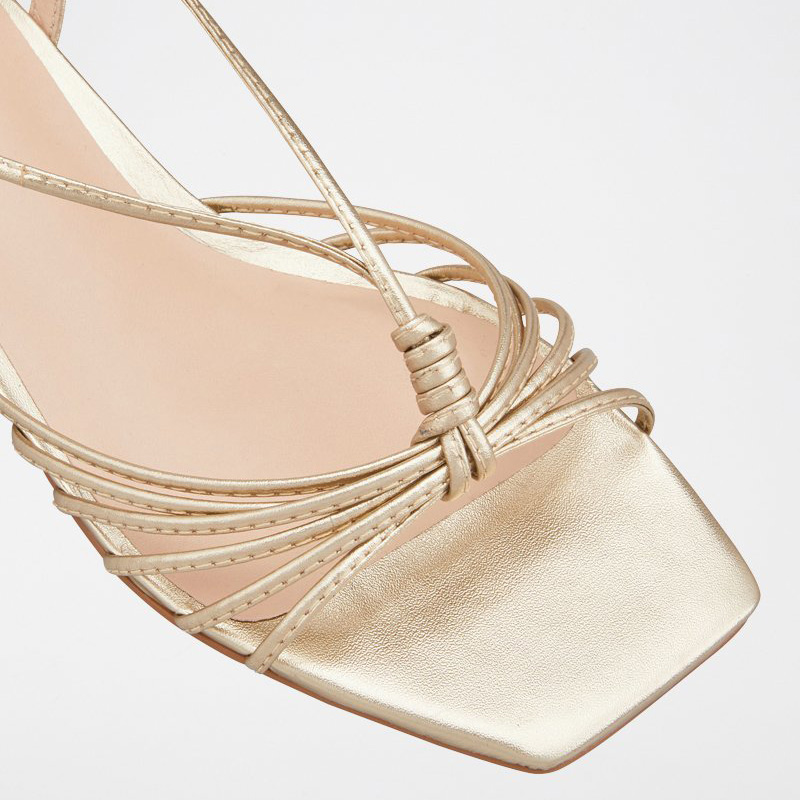 Sandália de salto dourada com tiras finas entrelaçadas e bico quadrado.