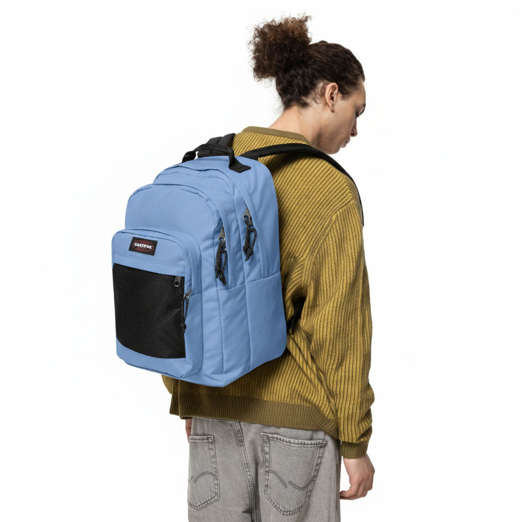 Mochila azul clara com bolso preto de rede usada por pessoa com camisola castanha e calças cinzentas.