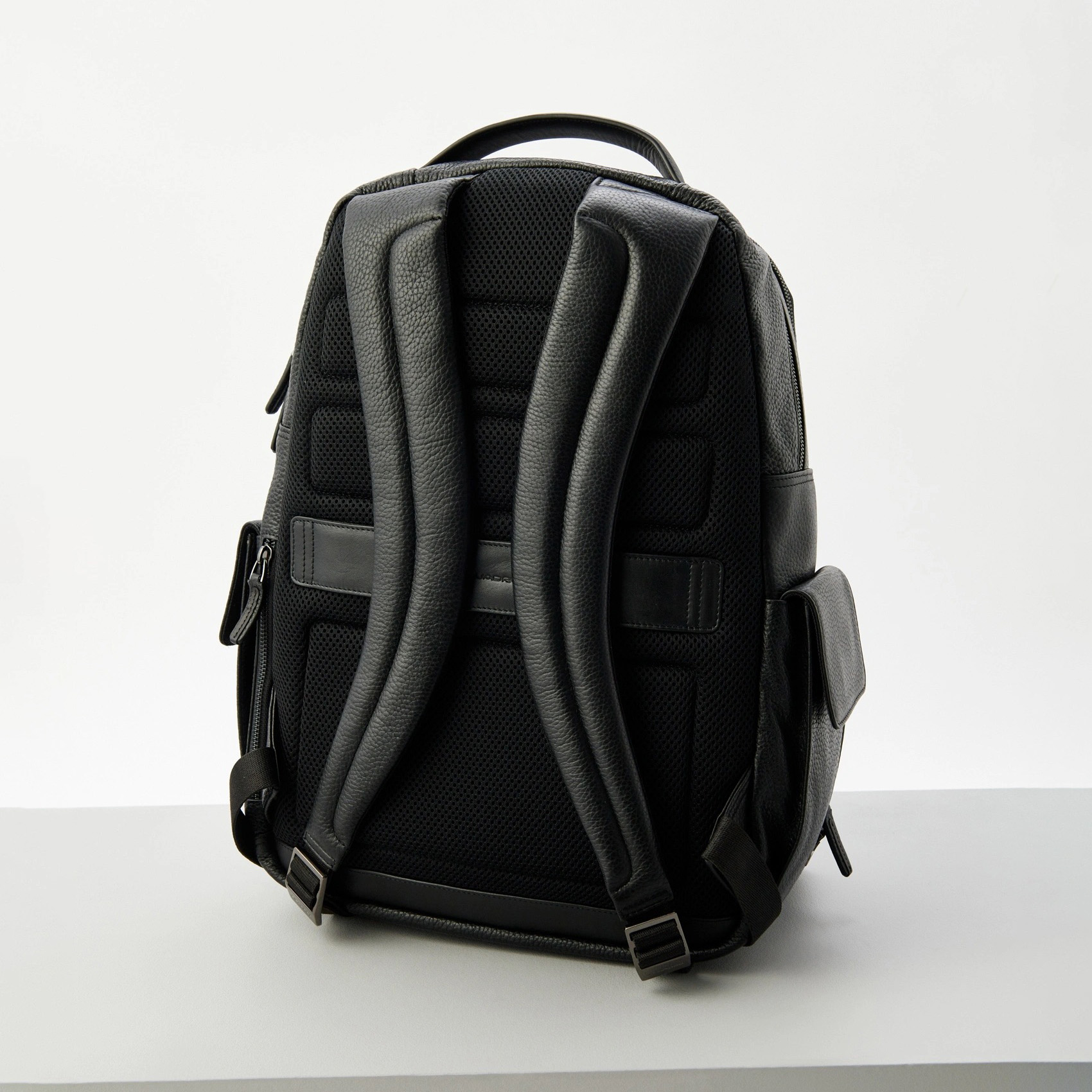 Mochila preta com alças acolchoadas e bolso lateral em fundo branco.