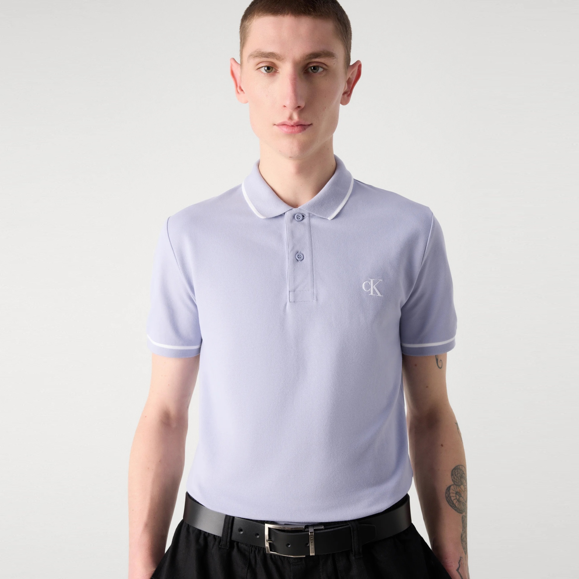 Polo lilás claro com gola e punhos brancos, logótipo cK bordado no peito, usado por homem
