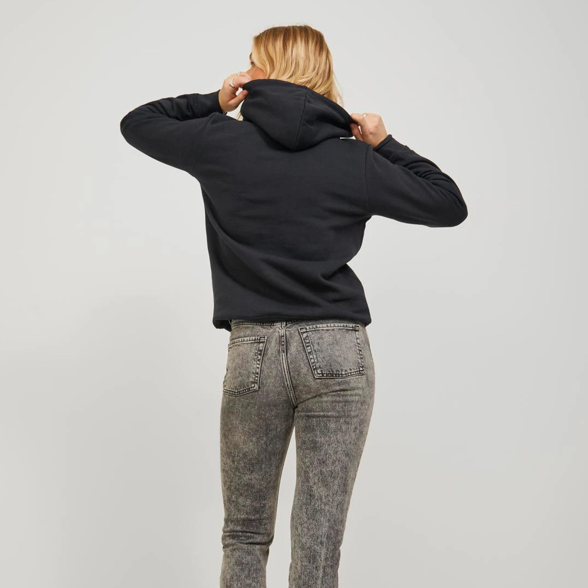 Mulher de costas a usar hoodie preto e calças de ganga cinza marmoreado