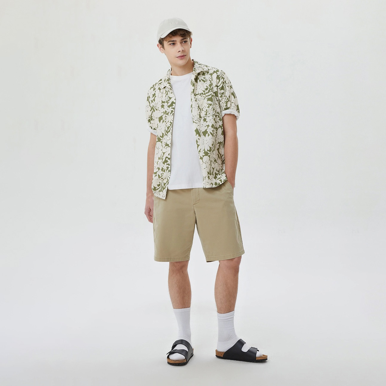 Homem com roupa casual usando chapéu, camisa floral, t-shirt, calções e sandálias