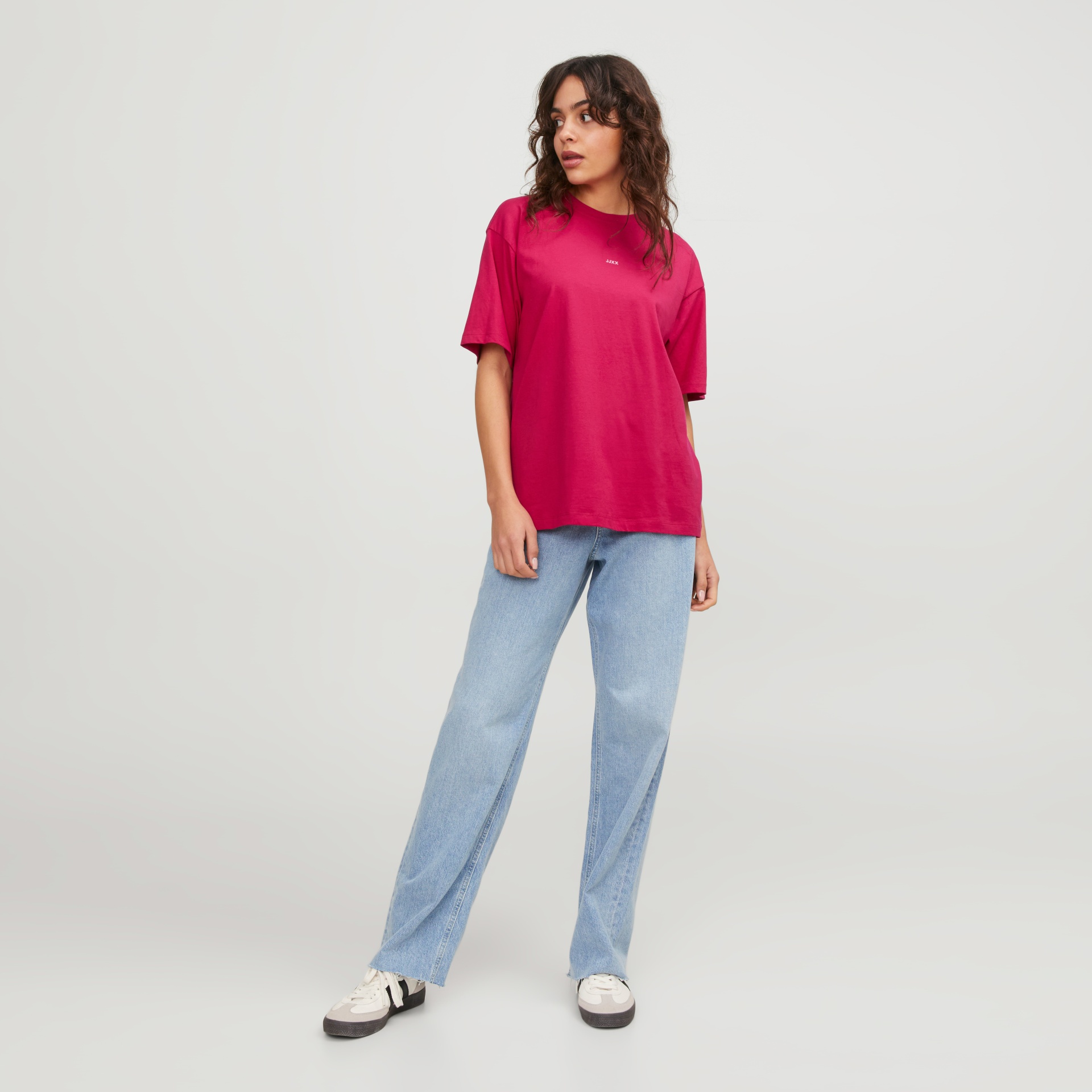 Mulher com t-shirt rosa e calças de ganga azuis em fundo branco