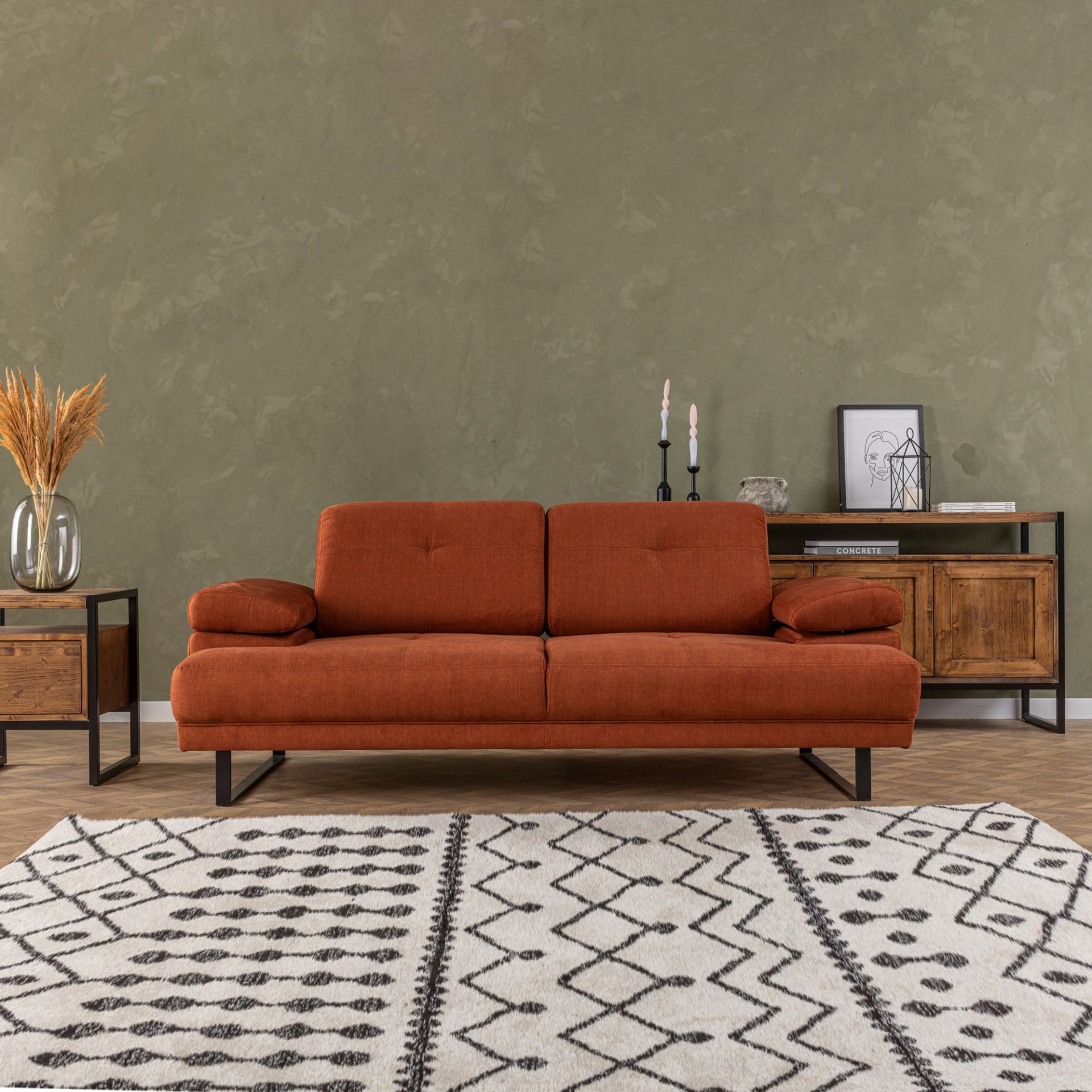 Sofá castanho avermelhado com pernas pretas numa sala com mesa lateral, aparador de madeira e tapete branco com padrões pretos
