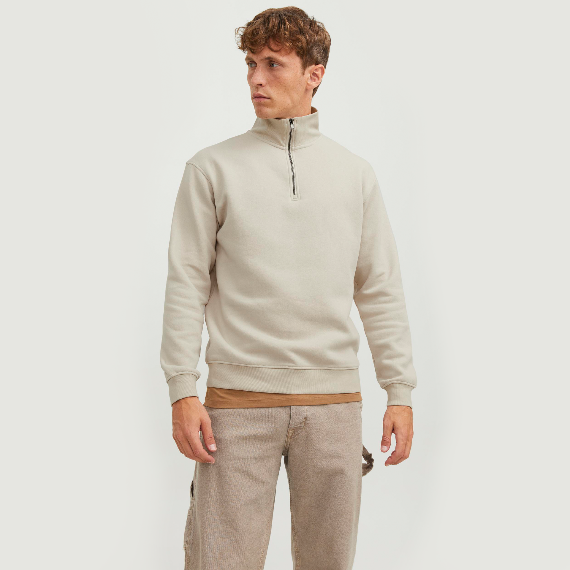 Homem com casaco bege de manga comprida com fecho na gola e calças castanhas claras