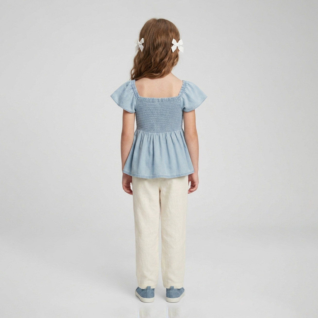 Criança de costas com blusa azul clara e calças bege
