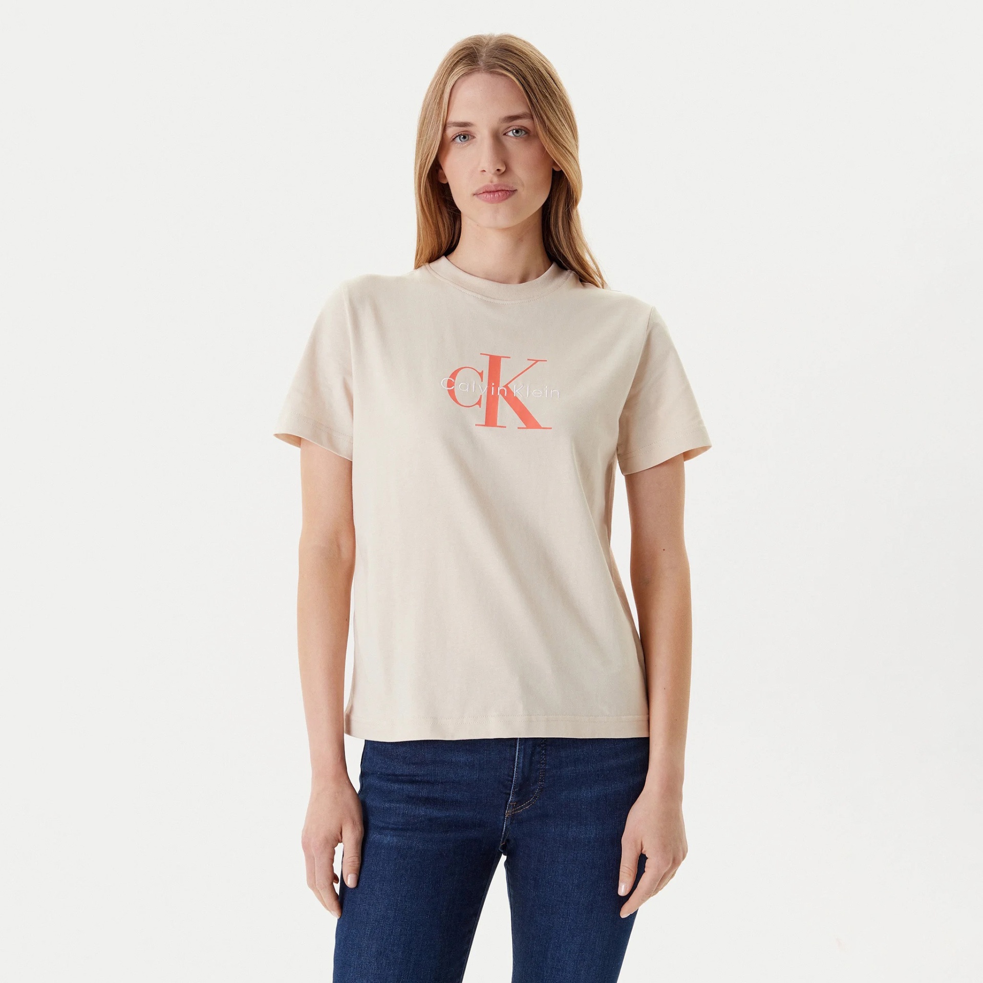 T-shirt bege com logo cK Calvin Klein em salmão, vista frontal, usada por mulher com jeans azul escuro