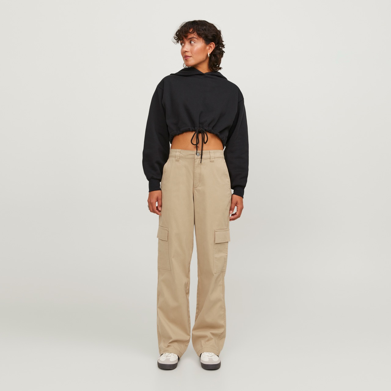 Mulher com calças largas bege e top preto curto com capuz