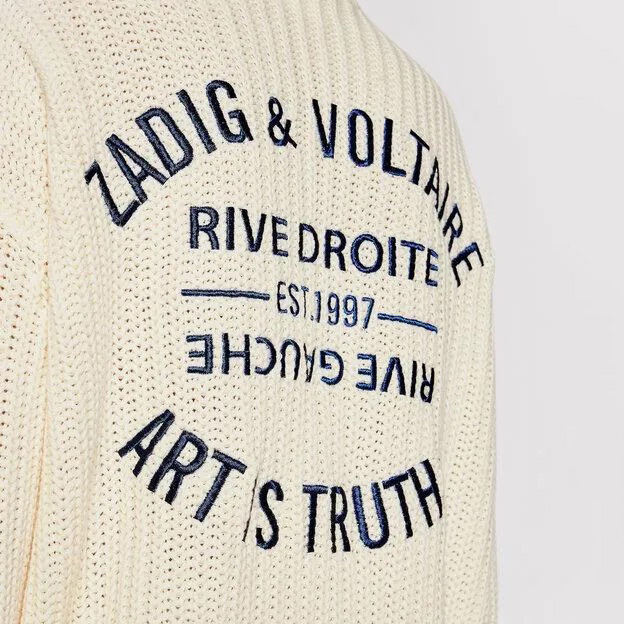 Suéter creme de malha grossa com bordados azuis e textos variados.