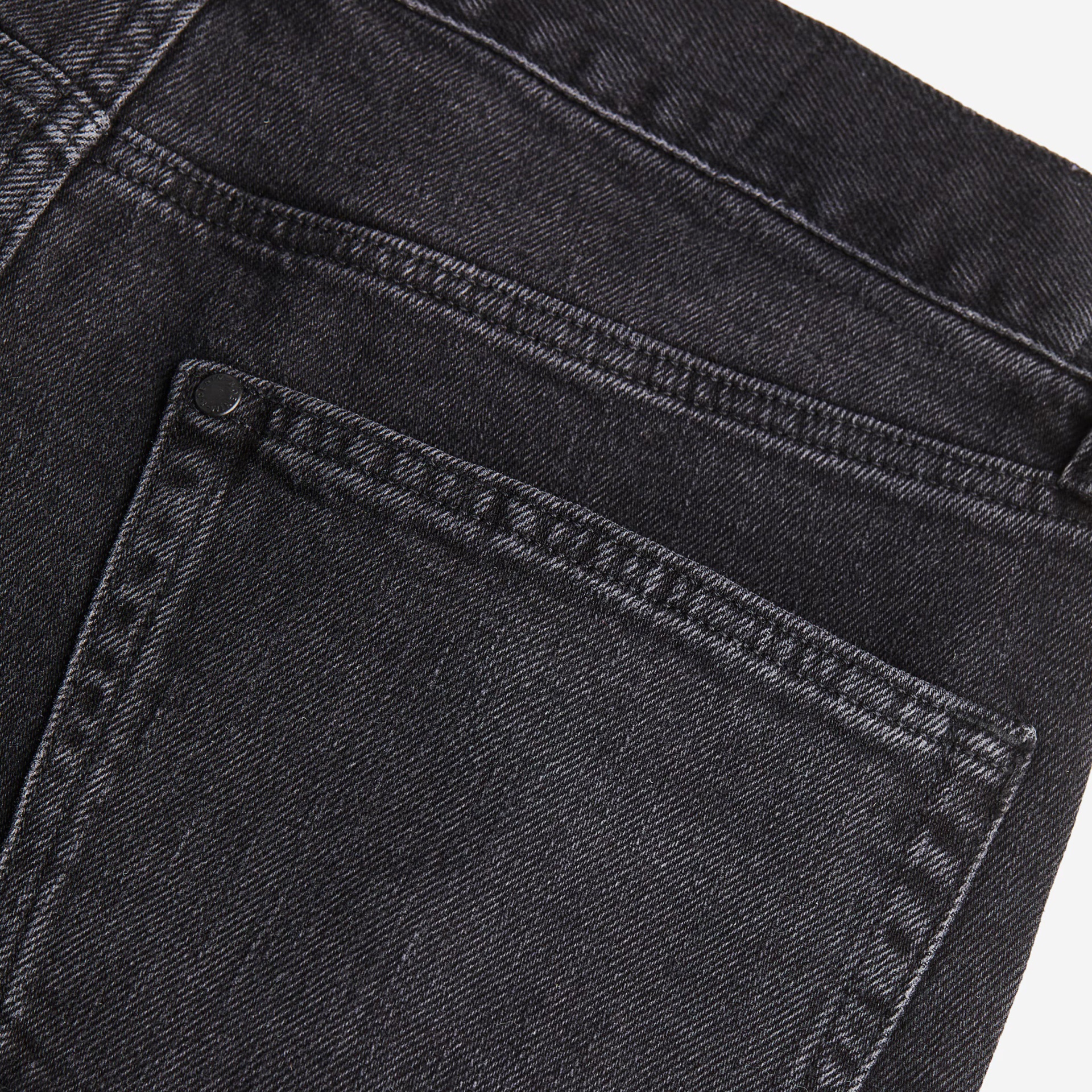 Pormenor de calça jeans preta em ganga com costuras e rebite